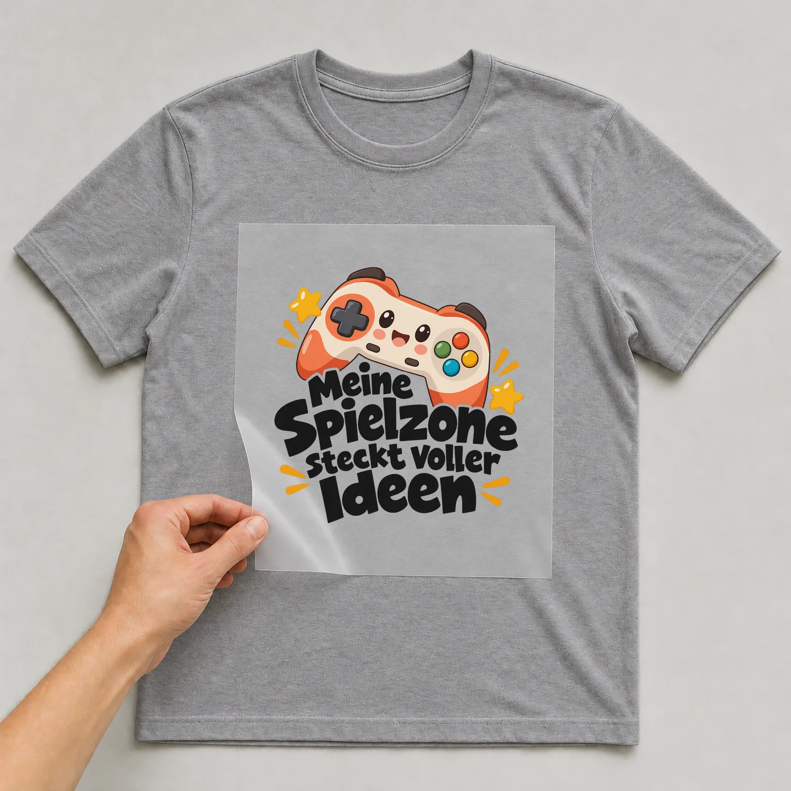 Bügelbild „Meine Spielzone steckt voller Ideen“ auf grauem T-Shirt, Folie wird aufgelegt