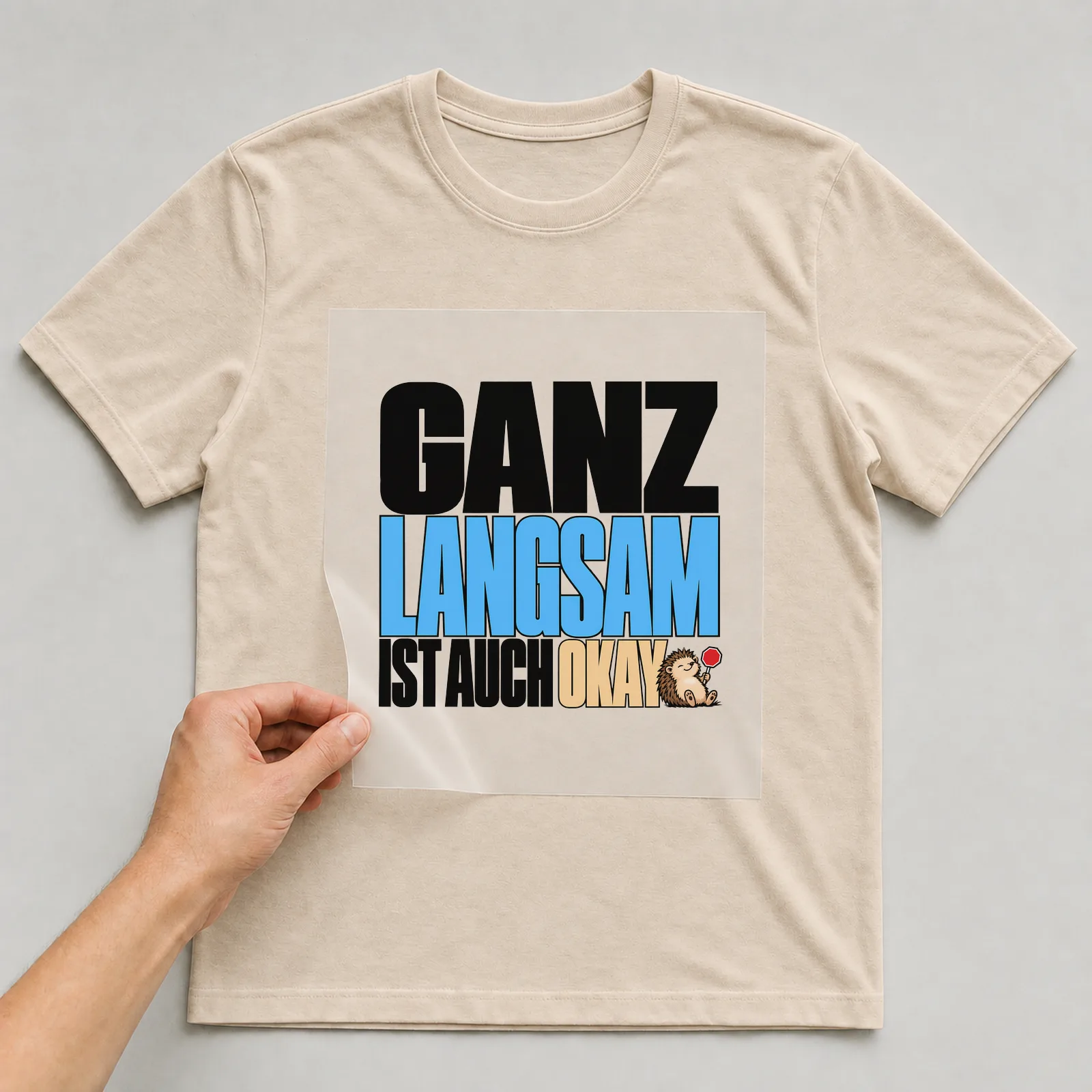 Bügelbild „Ganz langsam ist auch okay“ auf beigem T-Shirt, Folie wird aufgelegt