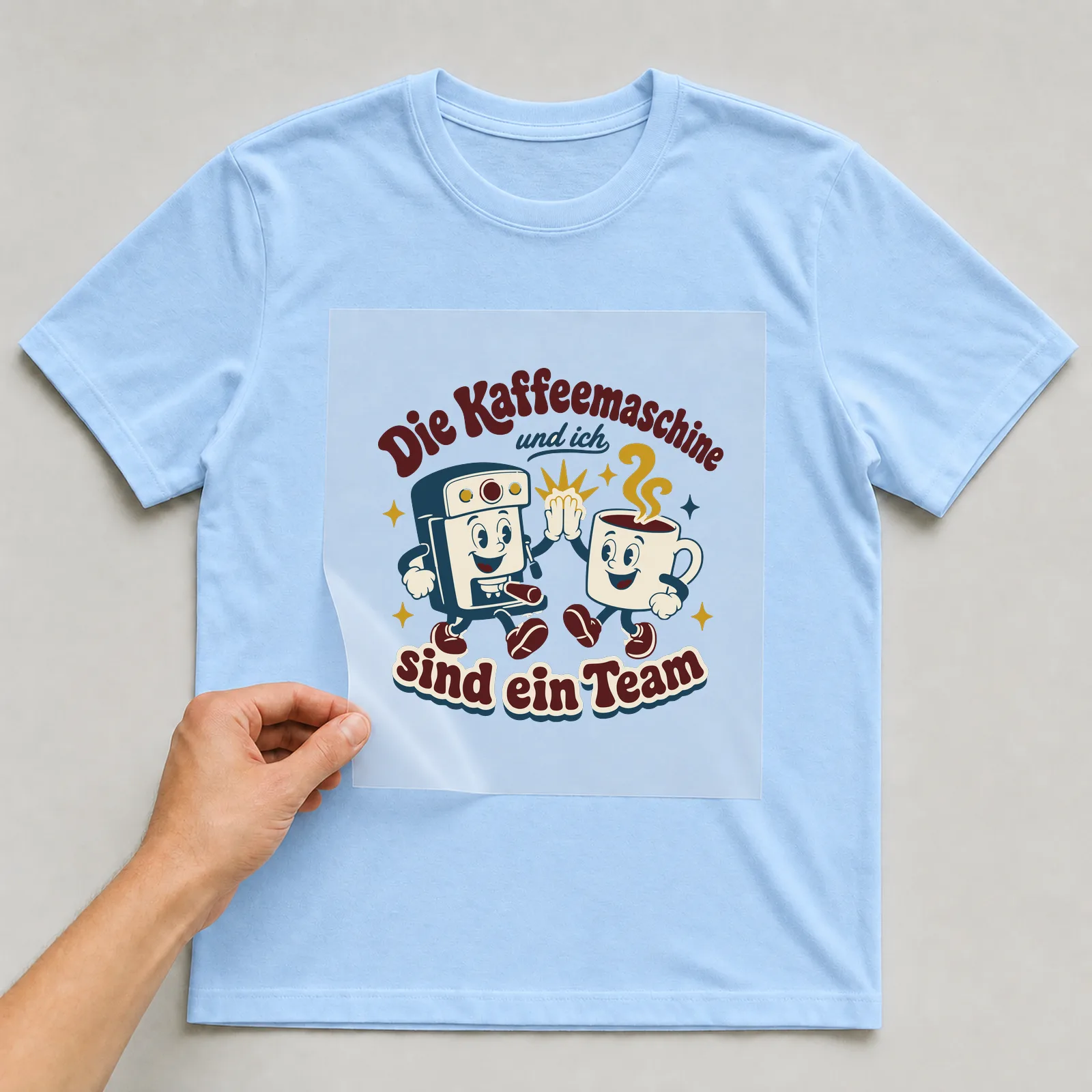 Bügelbild Die Kaffeemaschine und ich sind ein Team auf hellblauem T-Shirt, Folie wird aufgelegt
