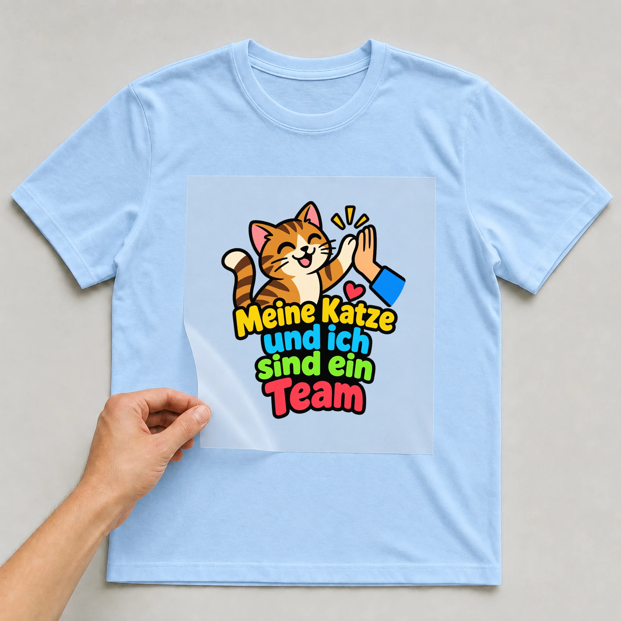 Bügelbild „Meine Katze und ich sind ein Team“ auf babyblauem T-Shirt, Folie wird aufgelegt
