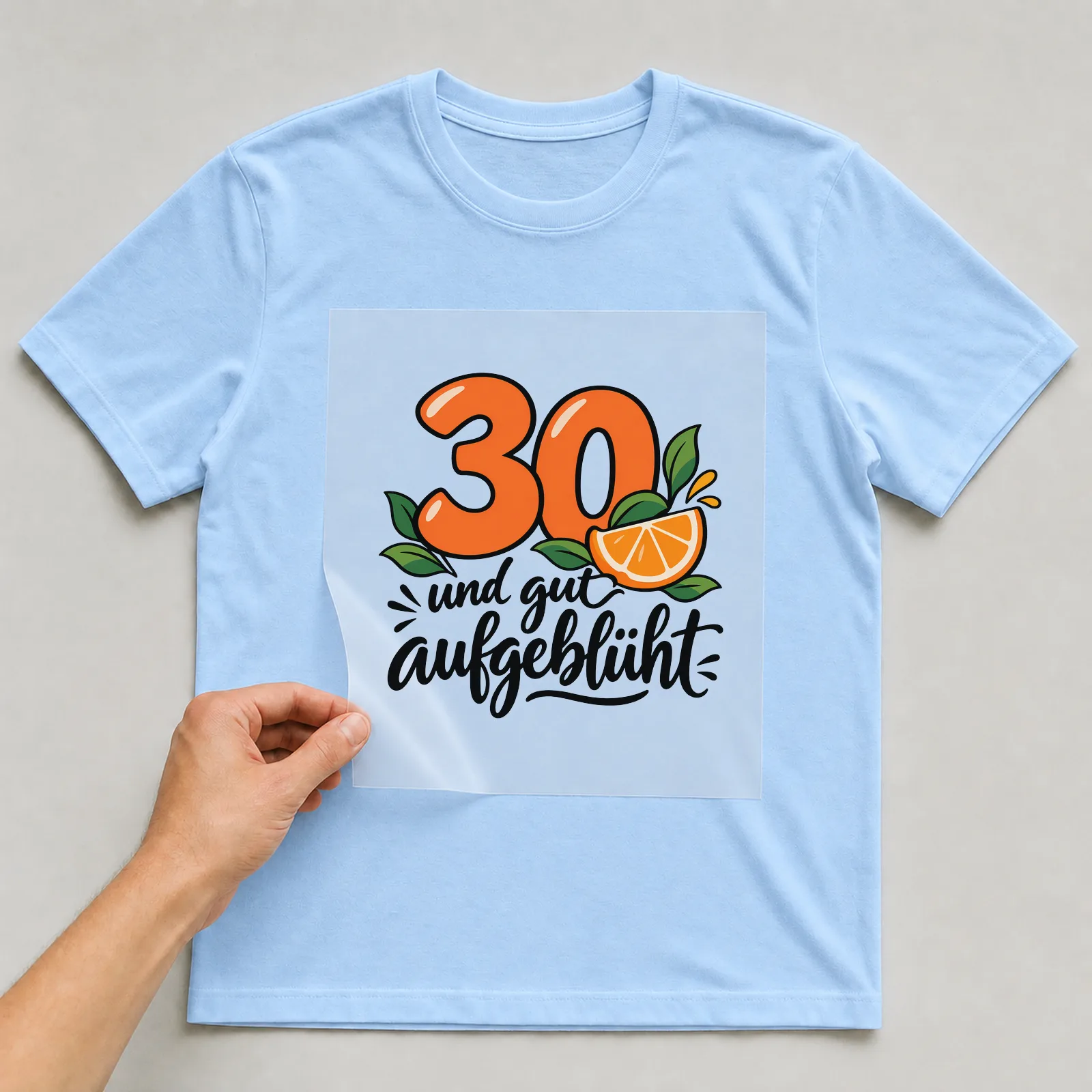 Bügelbild „30 und gut aufgeblüht“ auf hellblauem T-Shirt, Folie wird aufgelegt