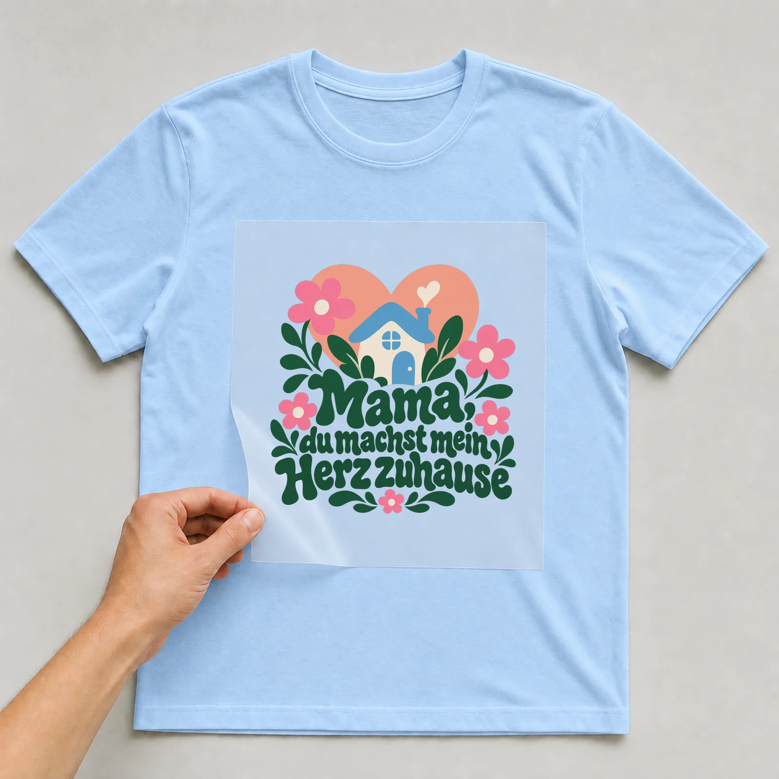 Bügelbild „Mama du machst mein Herz zuhause“ auf hellblauem T-Shirt, Folie wird aufgelegt