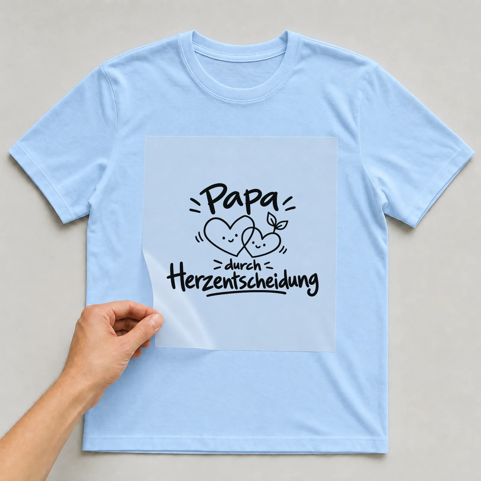 Bügelbild „Papa durch Herzentscheidung“ auf hellblauem T-Shirt, Folie wird aufgelegt
