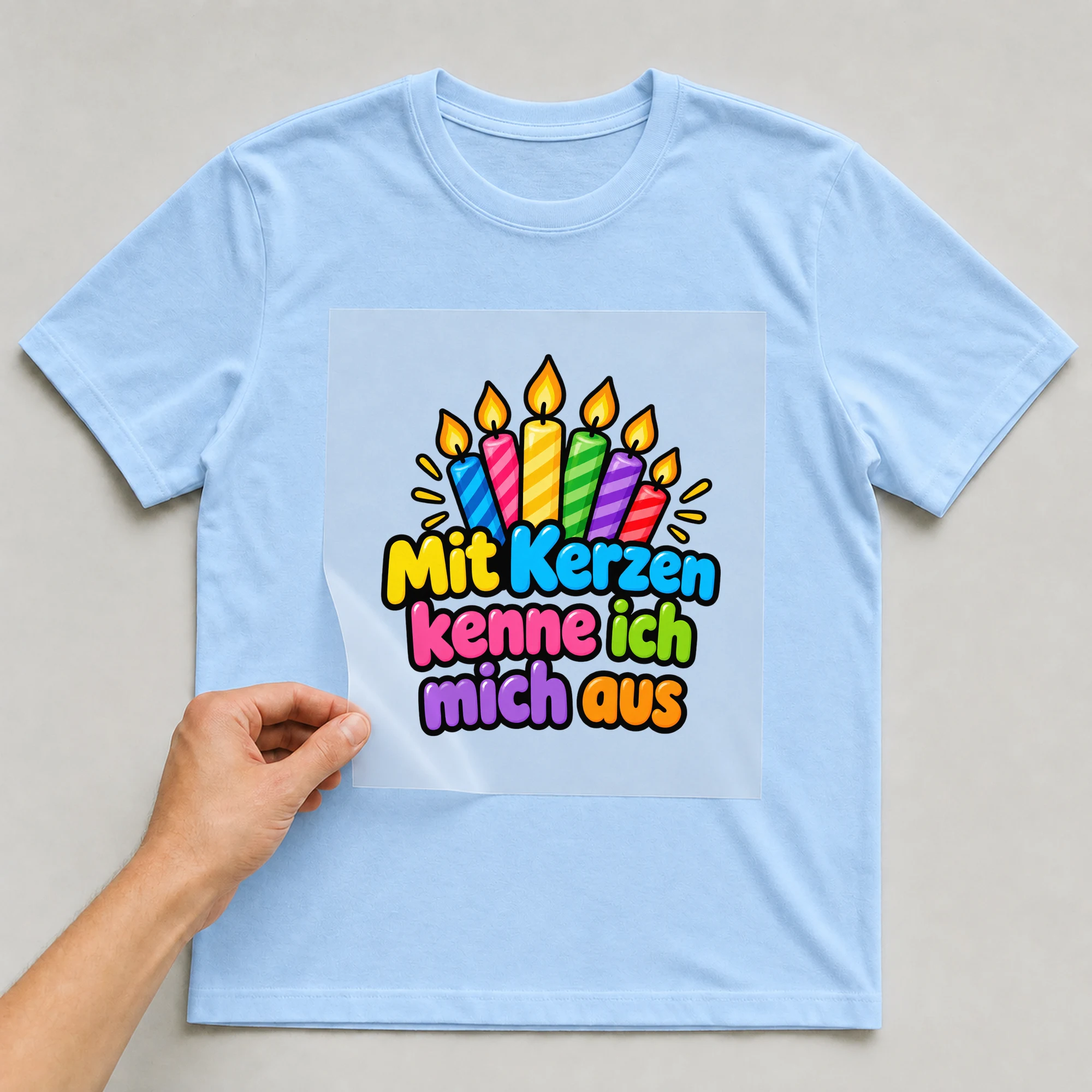 Bügelbild „Mit kerzen kenne ich mich aus“ auf babyblauem T-Shirt, Folie wird aufgelegt