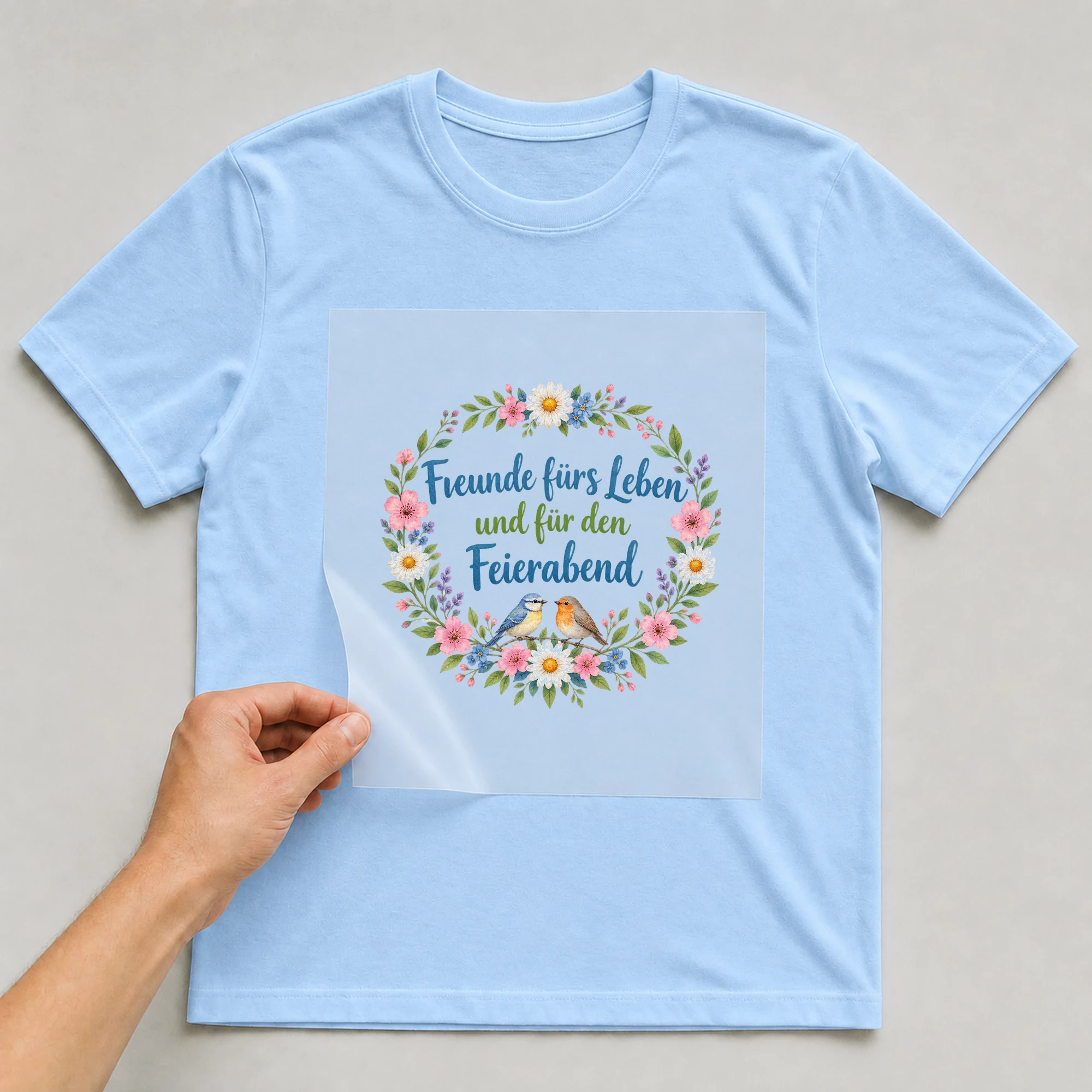 Bügelbild „Freunde fürs Leben und für den Feierabend“ auf babyblauem T-Shirt, Folie wird aufgelegt