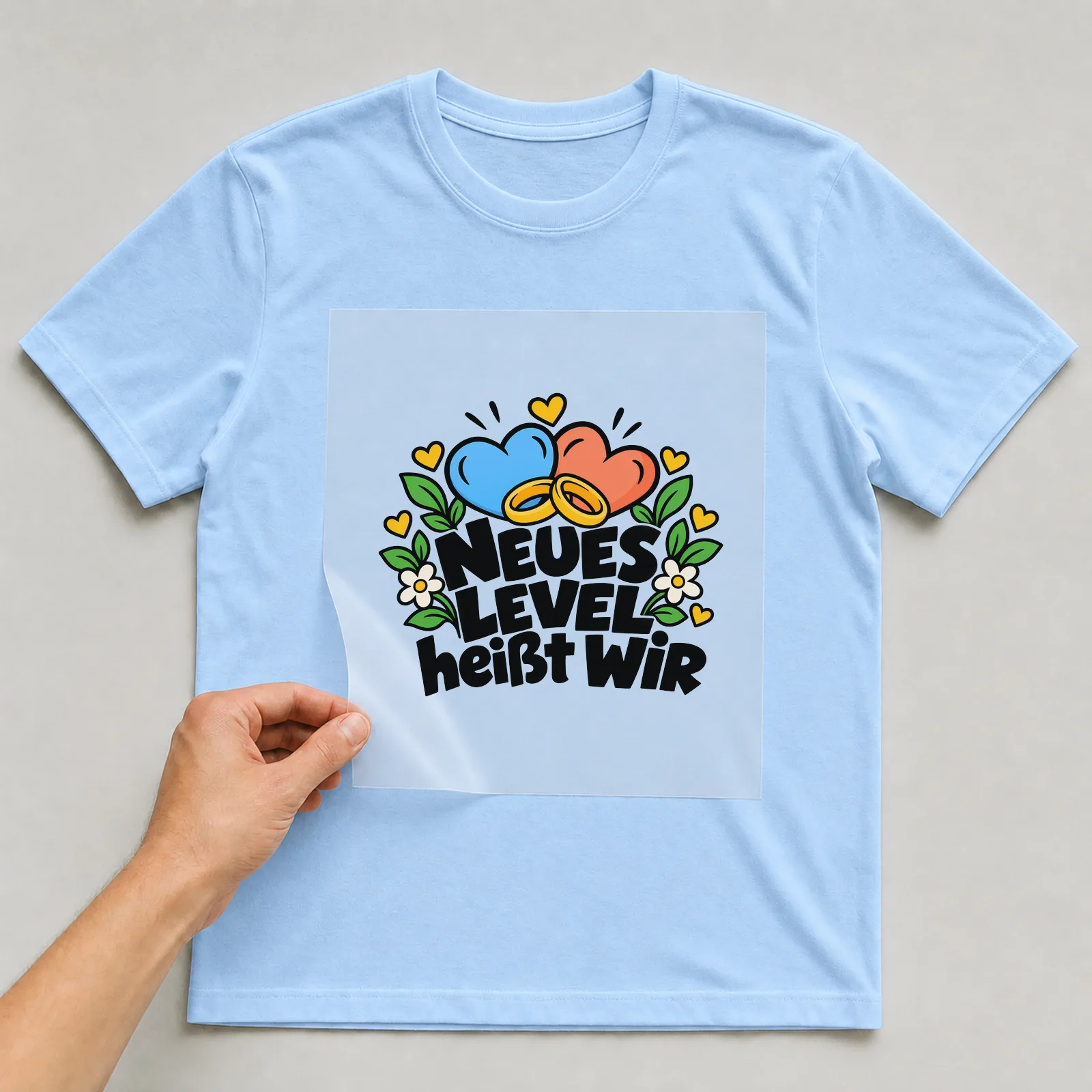 Bügelbild „NEUES LEVEL heißt WIR“ auf hellblauem T-Shirt, Folie wird aufgelegt
