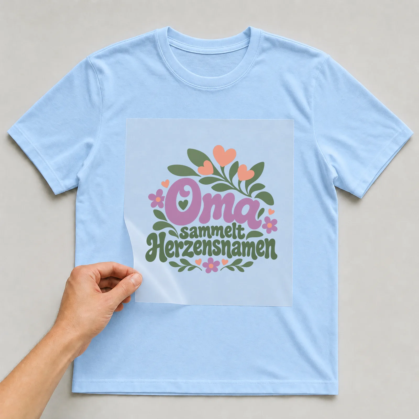 Bügelbild „Oma sammelt Herzensnamen“ auf hellblauem T-Shirt, Folie wird aufgelegt