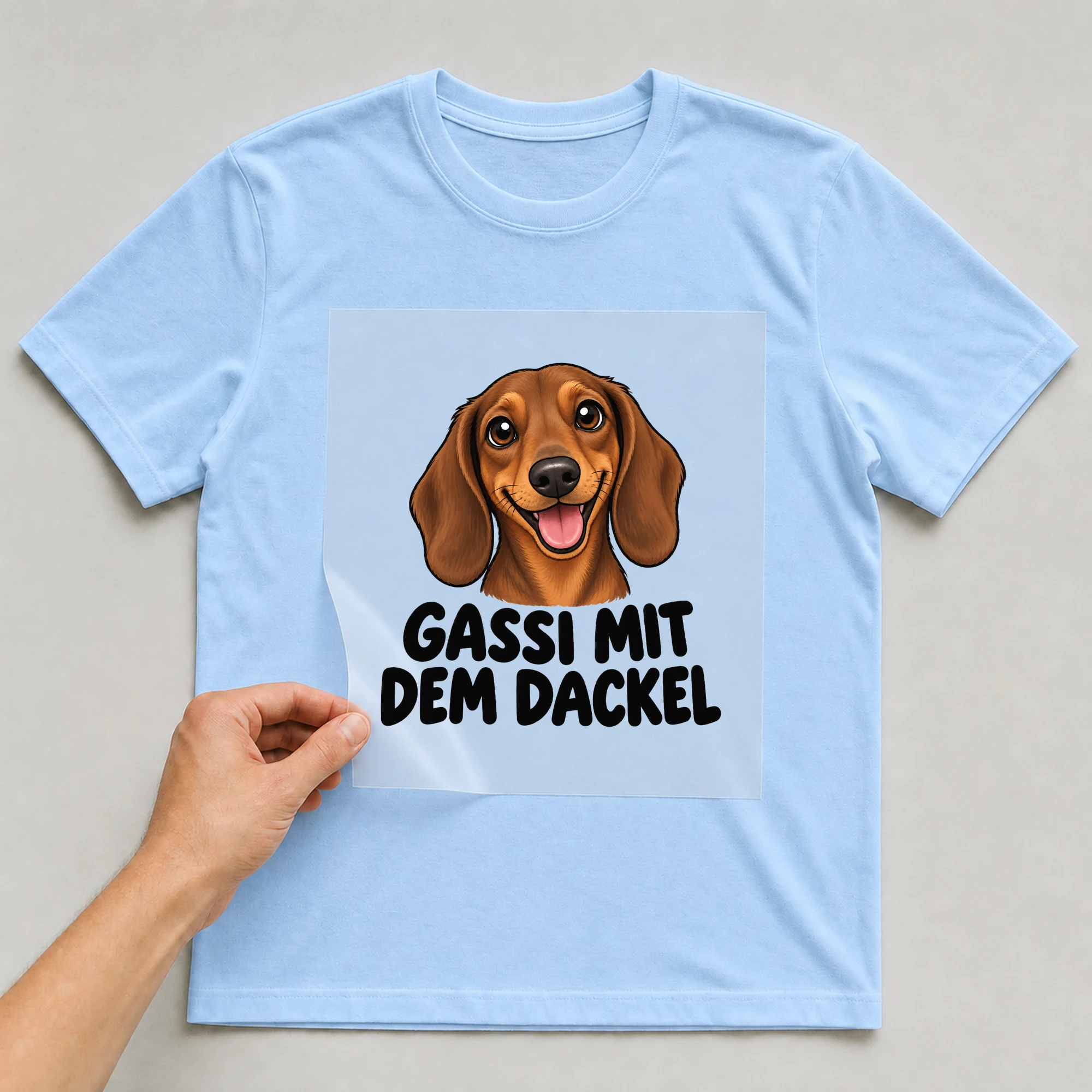 Bügelbild „Gassi mit dem Dackel“ auf babyblauem T-Shirt, Folie wird aufgelegt