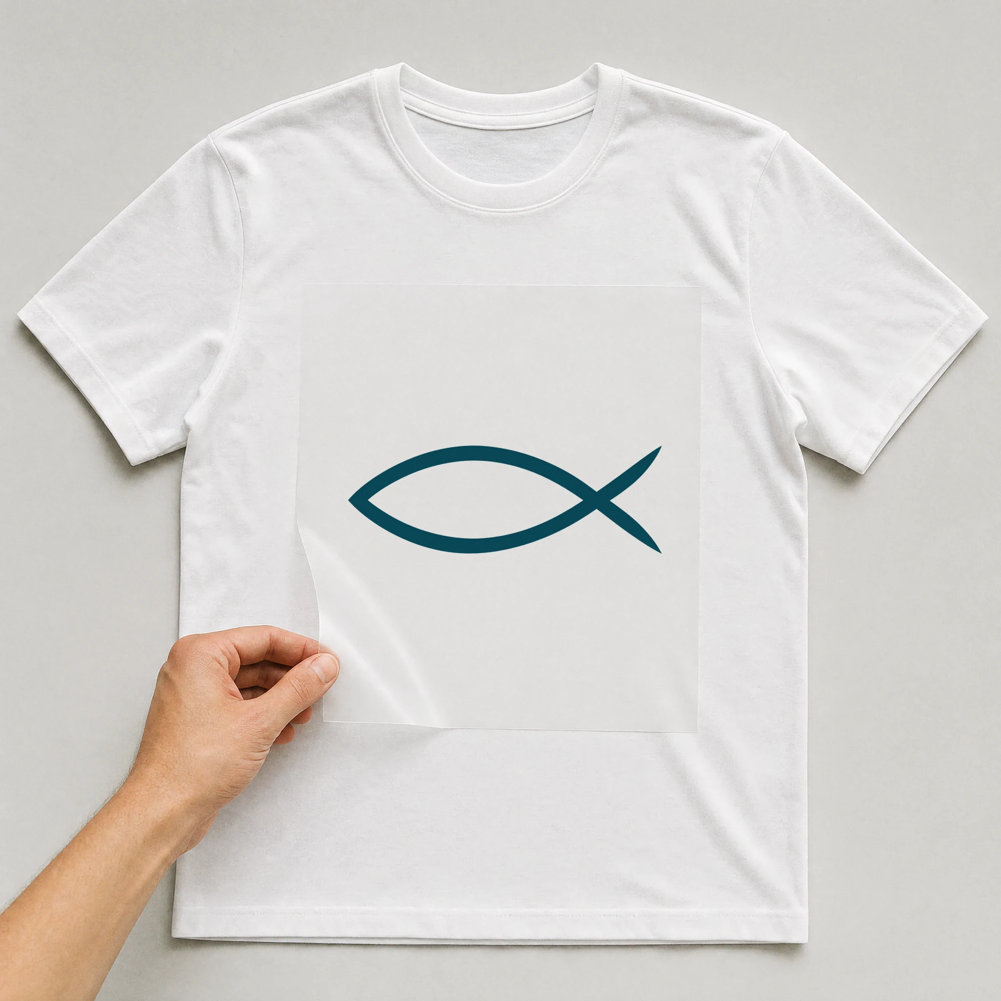 Bügelbild „Ichthys Fisch“ auf weißem T-Shirt, Folie wird aufgelegt