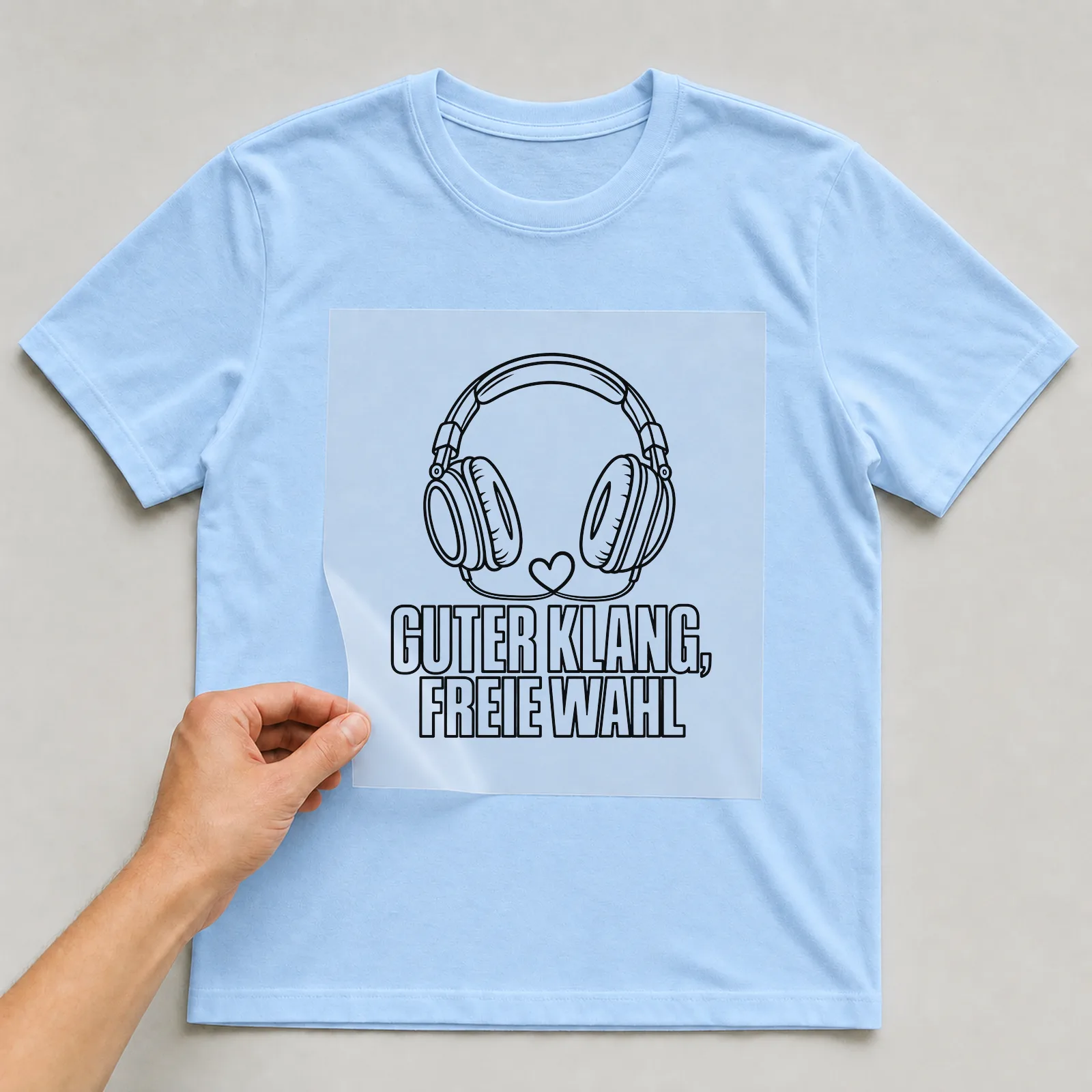 Bügelbild „Guter klang, freie Wahl“ auf hellblauem T-Shirt, Folie wird aufgelegt