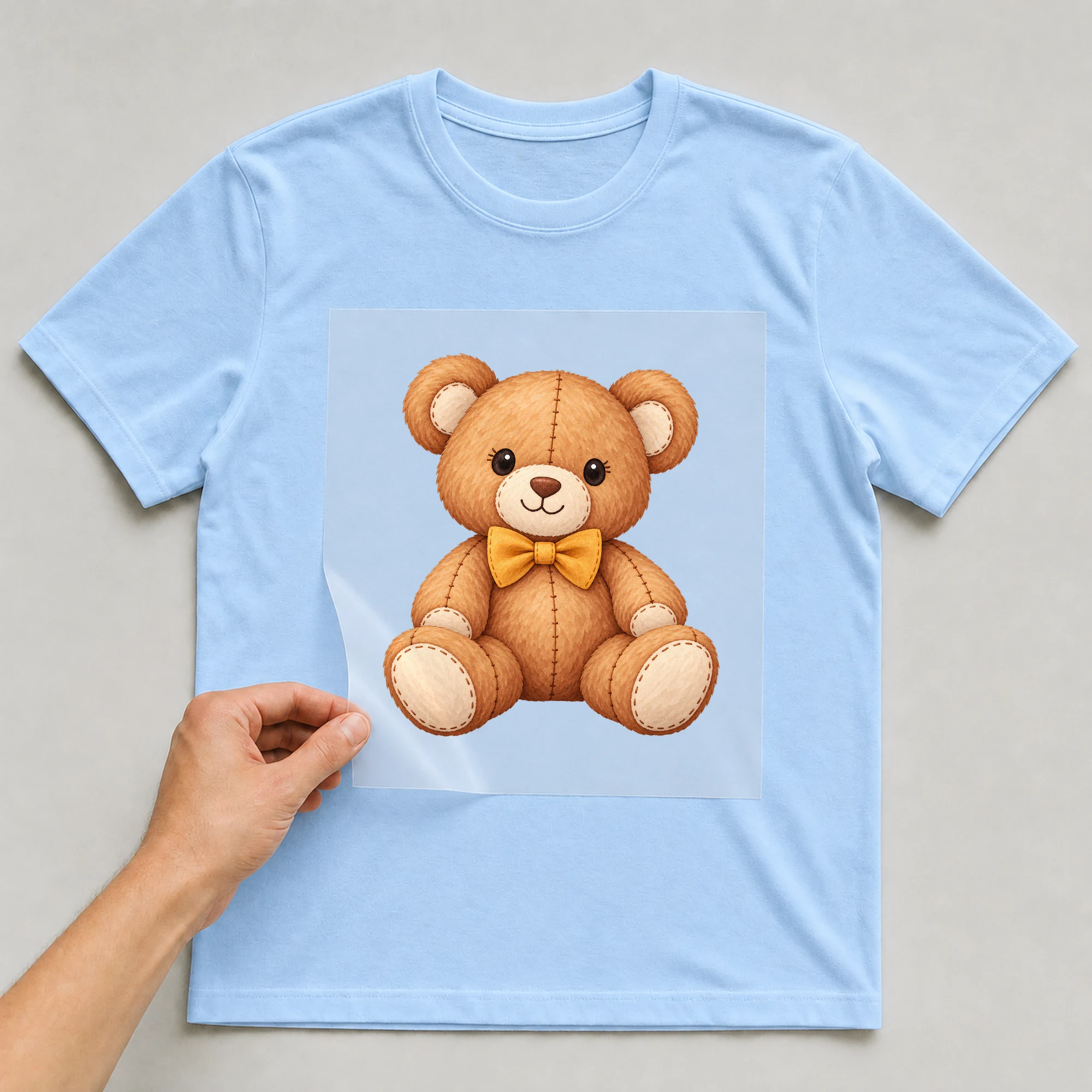 Bügelbild „Baby Comic - Bär“ auf babyblauem T-Shirt, Folie wird aufgelegt