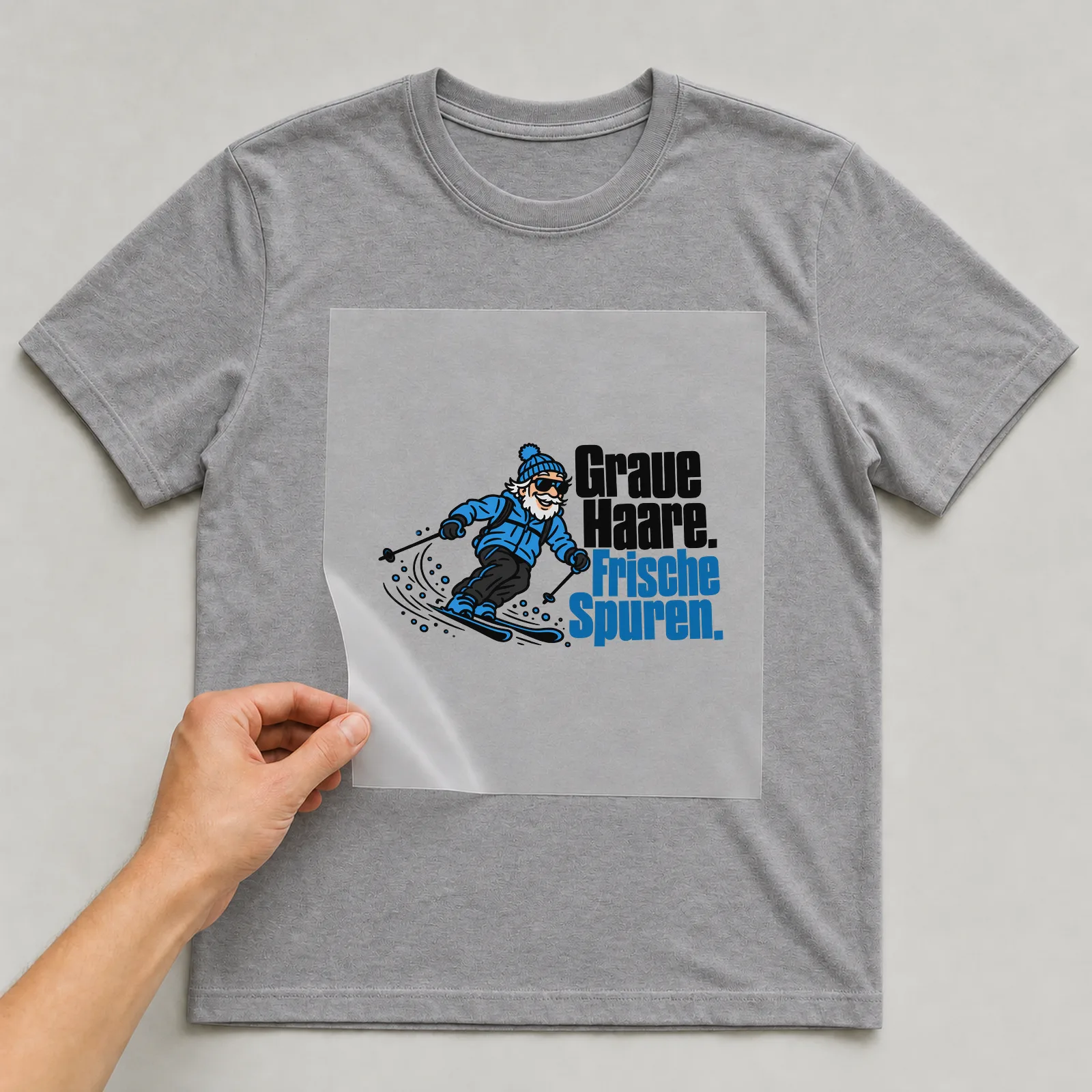 Bügelbild „Graue Haare. Frische Spuren.“ auf grauem T-Shirt, Folie wird aufgelegt