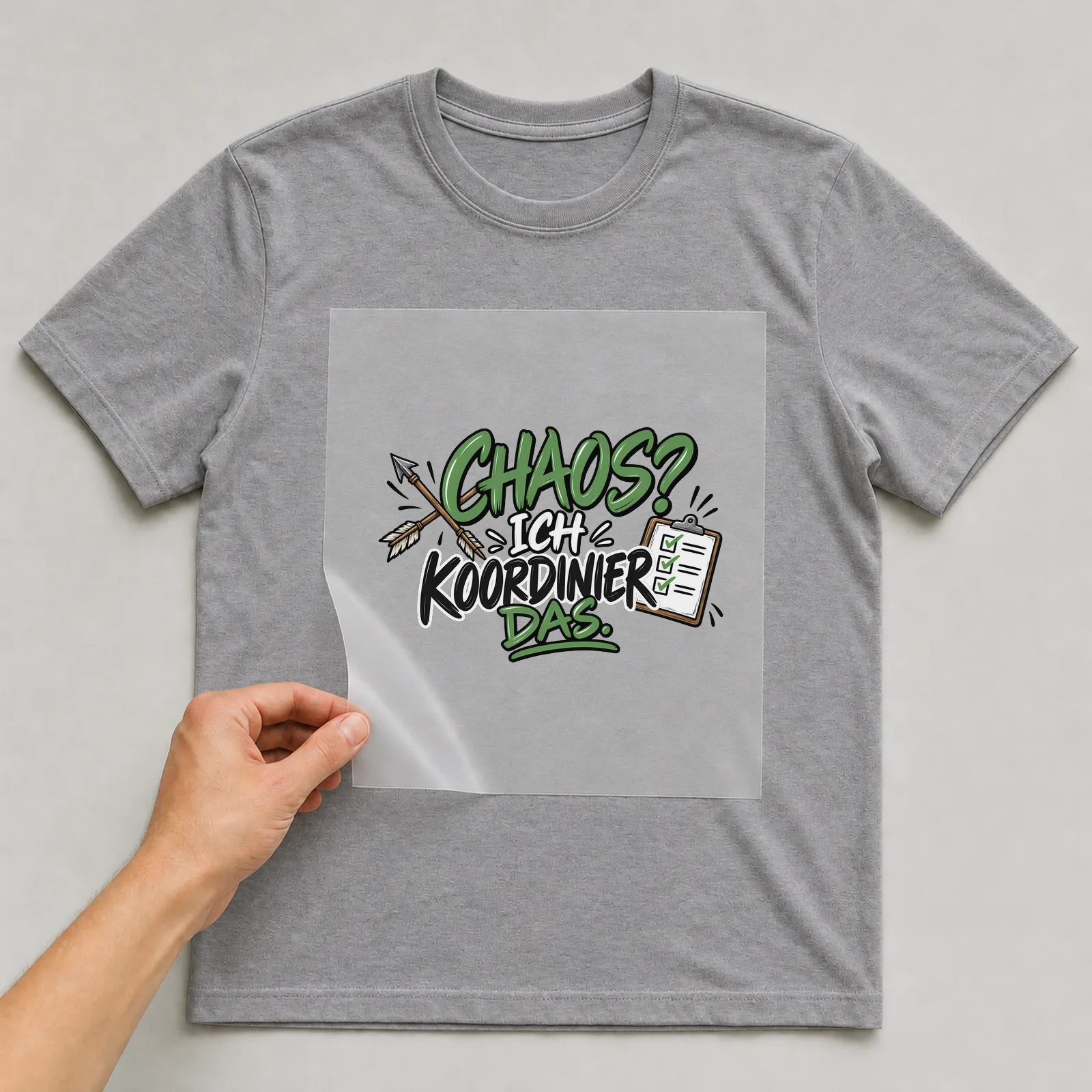 Bügelbild „Chaos? Ich koordinier das.“ auf grauem T-Shirt, Folie wird aufgelegt
