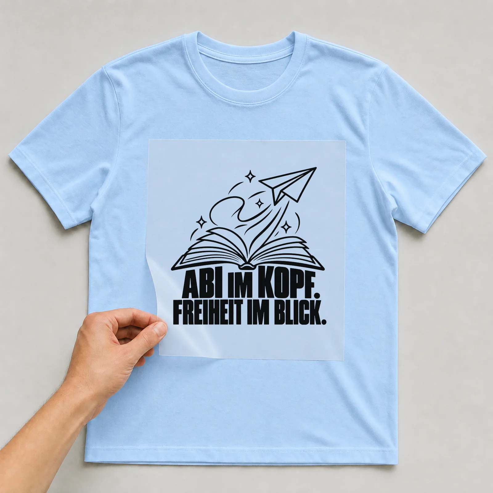 Bügelbild „Abi im Kopf. Freiheit im Blick.“ auf hellblauem T-Shirt, Folie wird aufgelegt