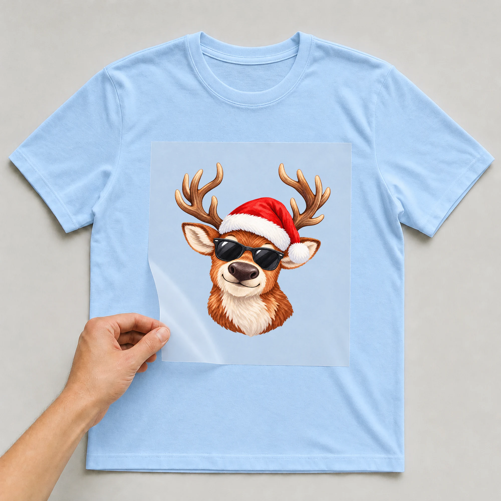 Bügelbild „Cooles Weihnachtsmann-Rentier“ auf babyblauem T-Shirt, Folie wird aufgelegt