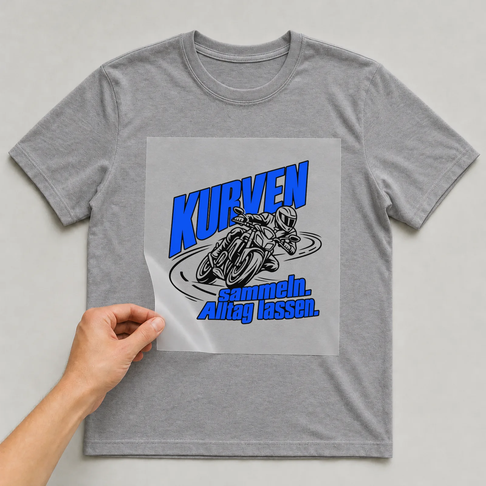 Bügelbild „Kurven sammeln. Alltag lassen.“ auf grauem T-Shirt, Folie wird aufgelegt