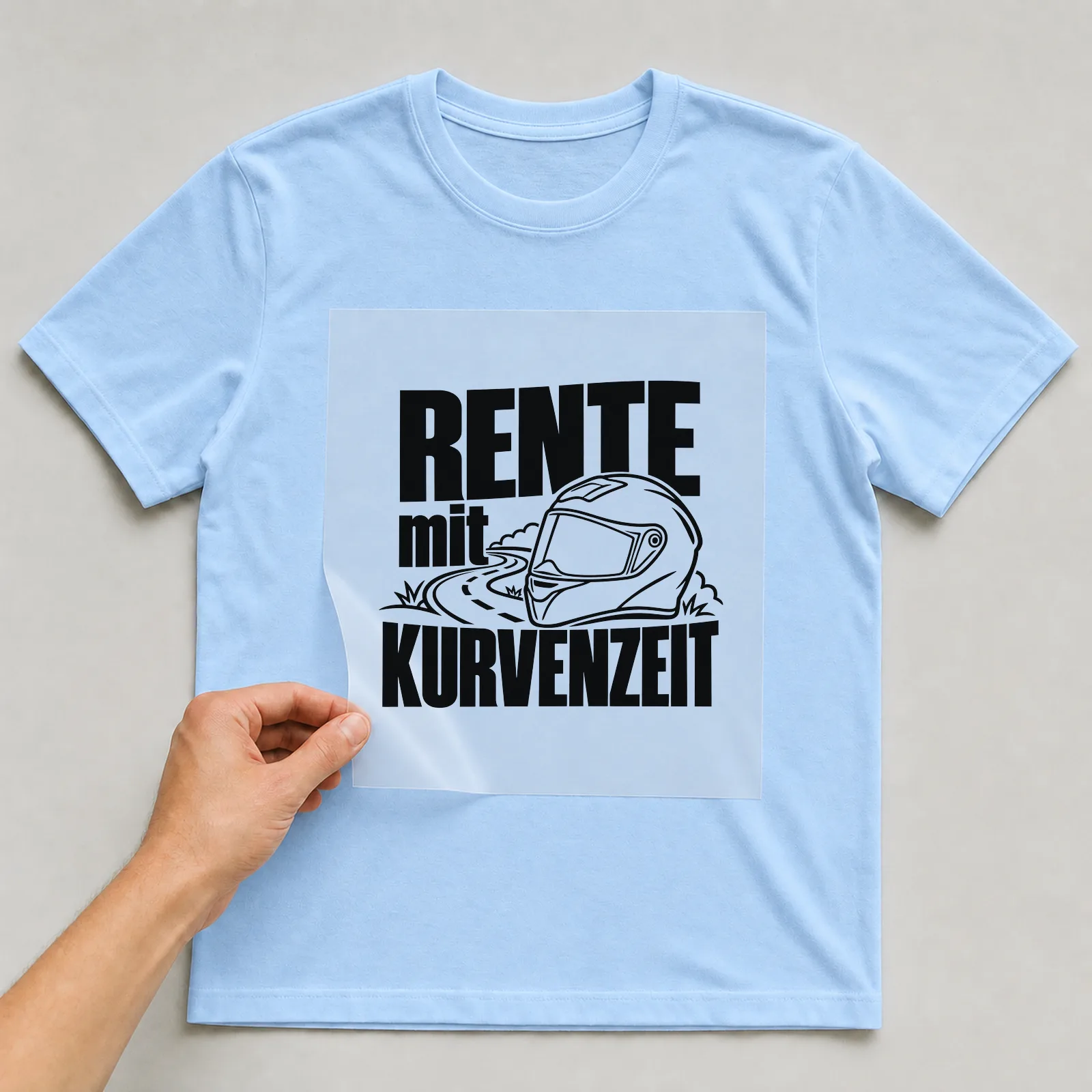 Bügelbild „Rente mit Kurvenzeit“ auf hellblauem T-Shirt, Folie wird aufgelegt