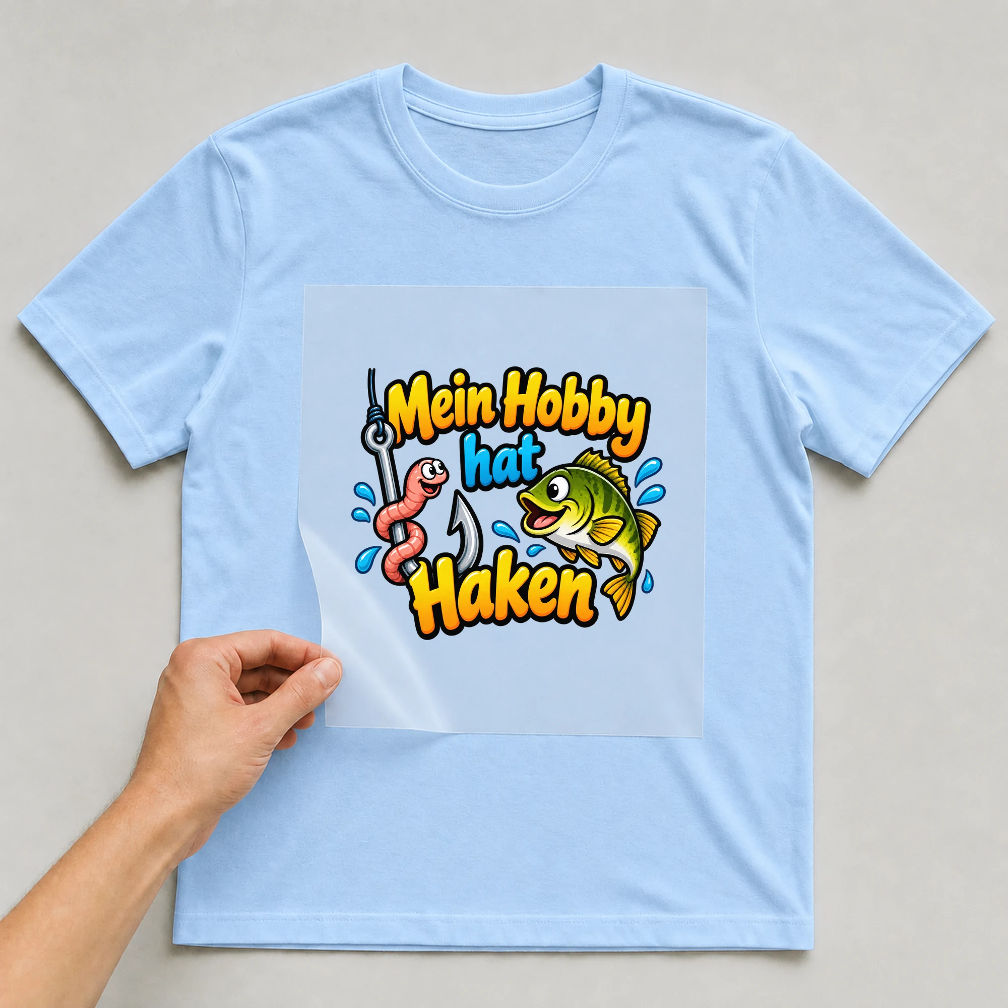 Bügelbild „Mein Hobby hat Haken“ auf babyblauem T-Shirt, Folie wird aufgelegt