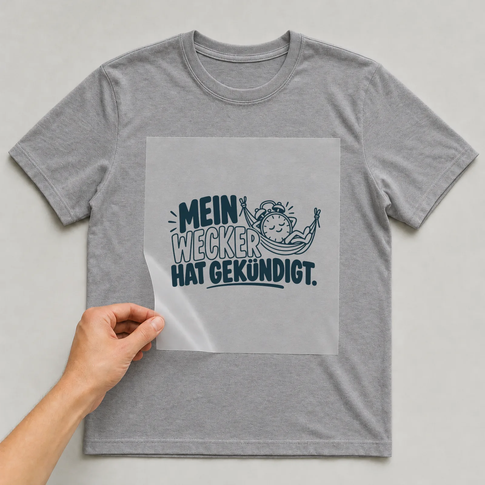 Bügelbild „Mein Wecker hat gekündigt“ auf grauem T-Shirt, Folie wird aufgelegt