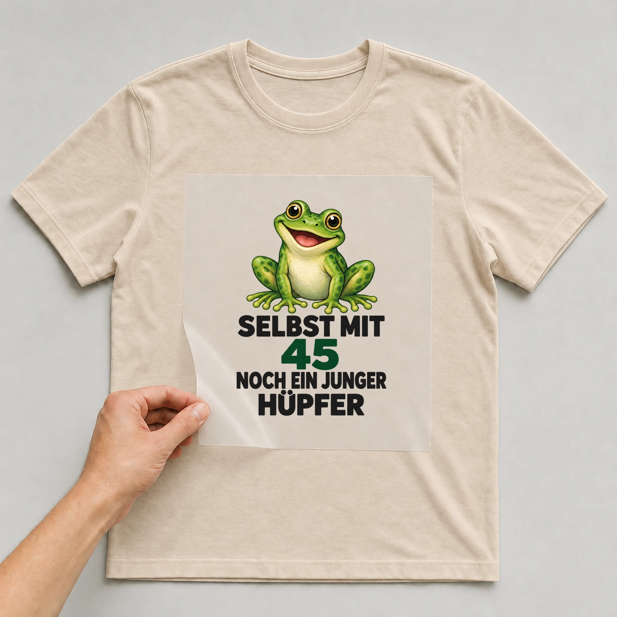 Bügelbild „Selbst mit 45 noch ein junger Hüpfer“ auf beigem T-Shirt, Folie wird aufgelegt
