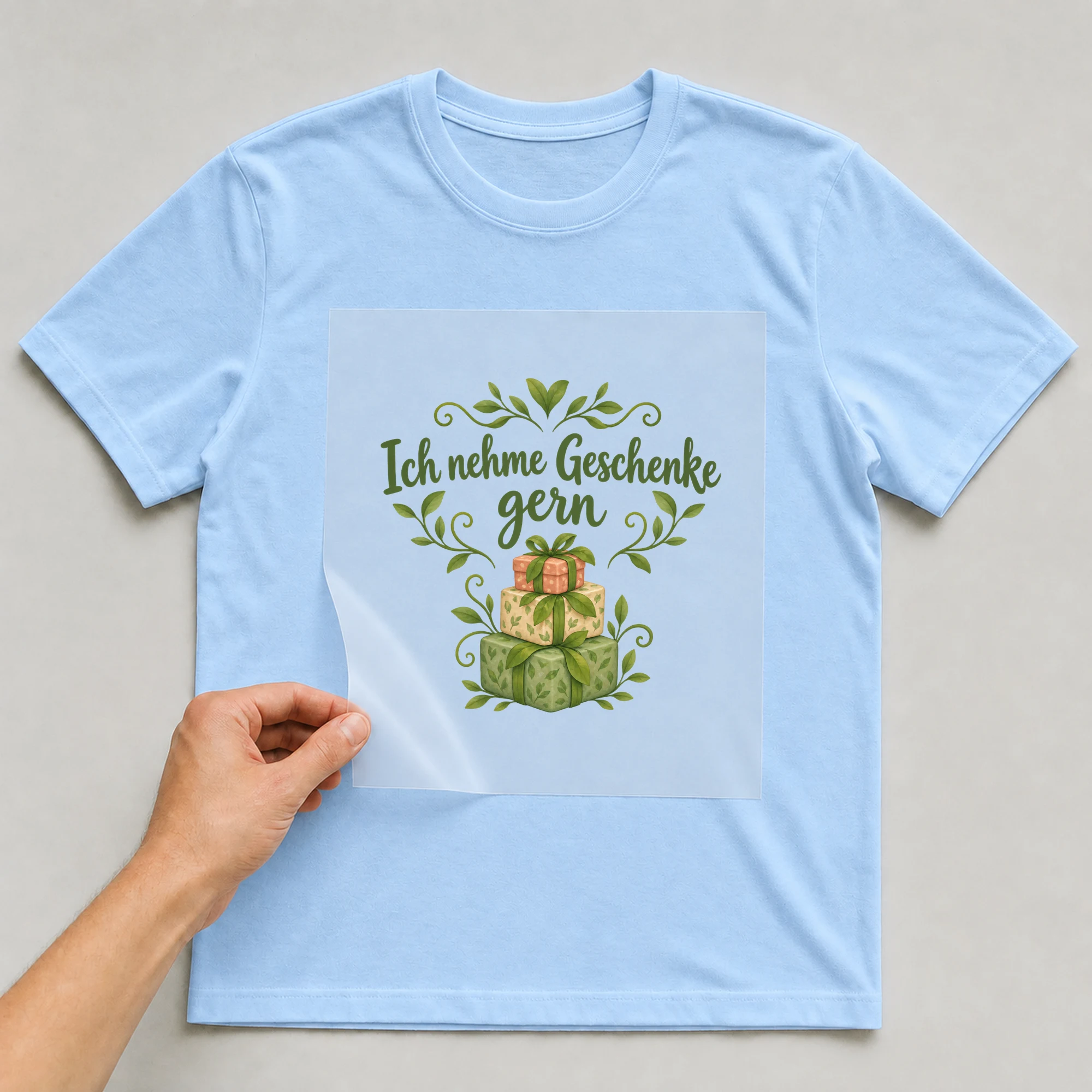 Bügelbild „Ich nehme Geschenke gern“ auf babyblauem T-Shirt, Folie wird aufgelegt