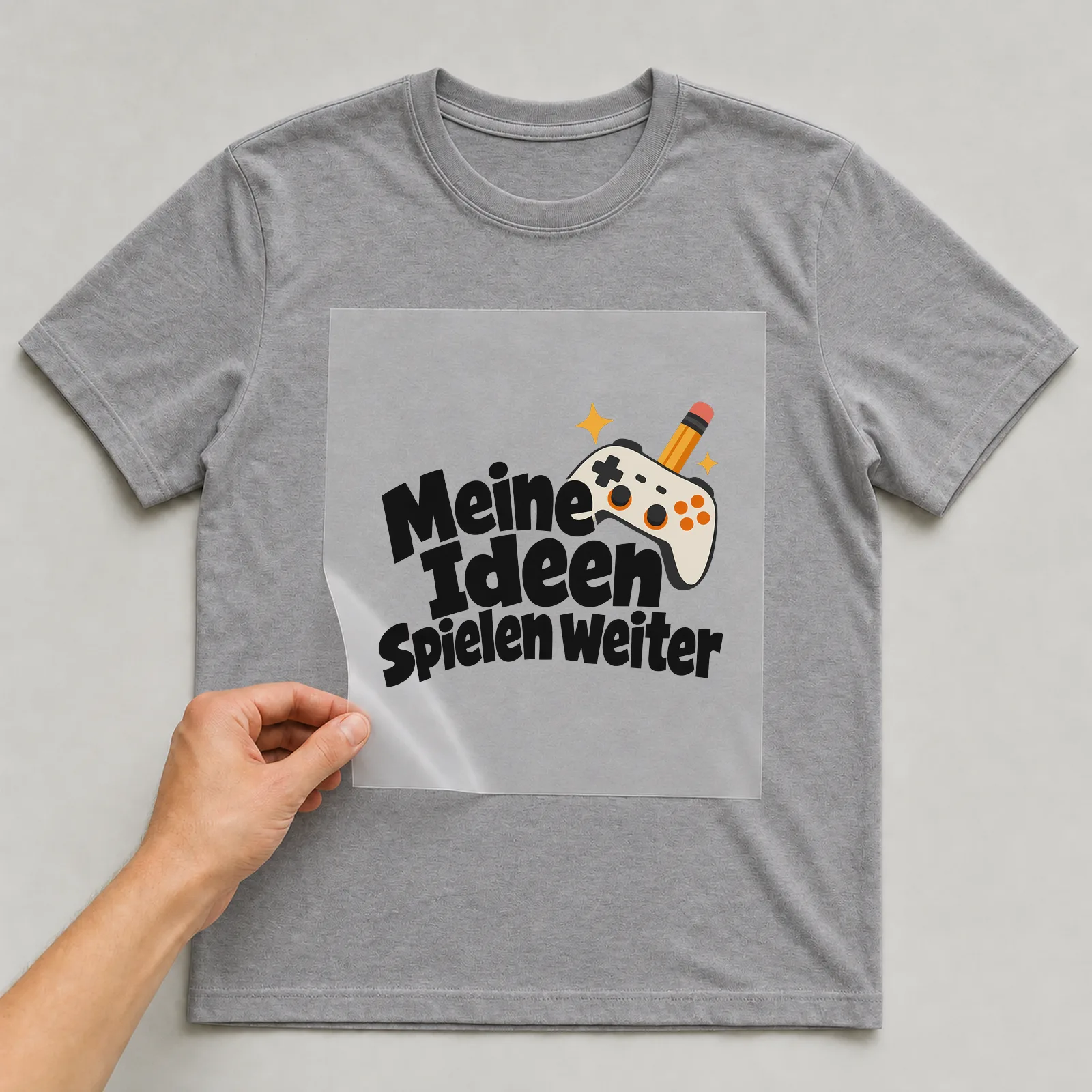 Bügelbild „Meine Ideen spielen weiter“ auf grauem T-Shirt, Folie wird aufgelegt