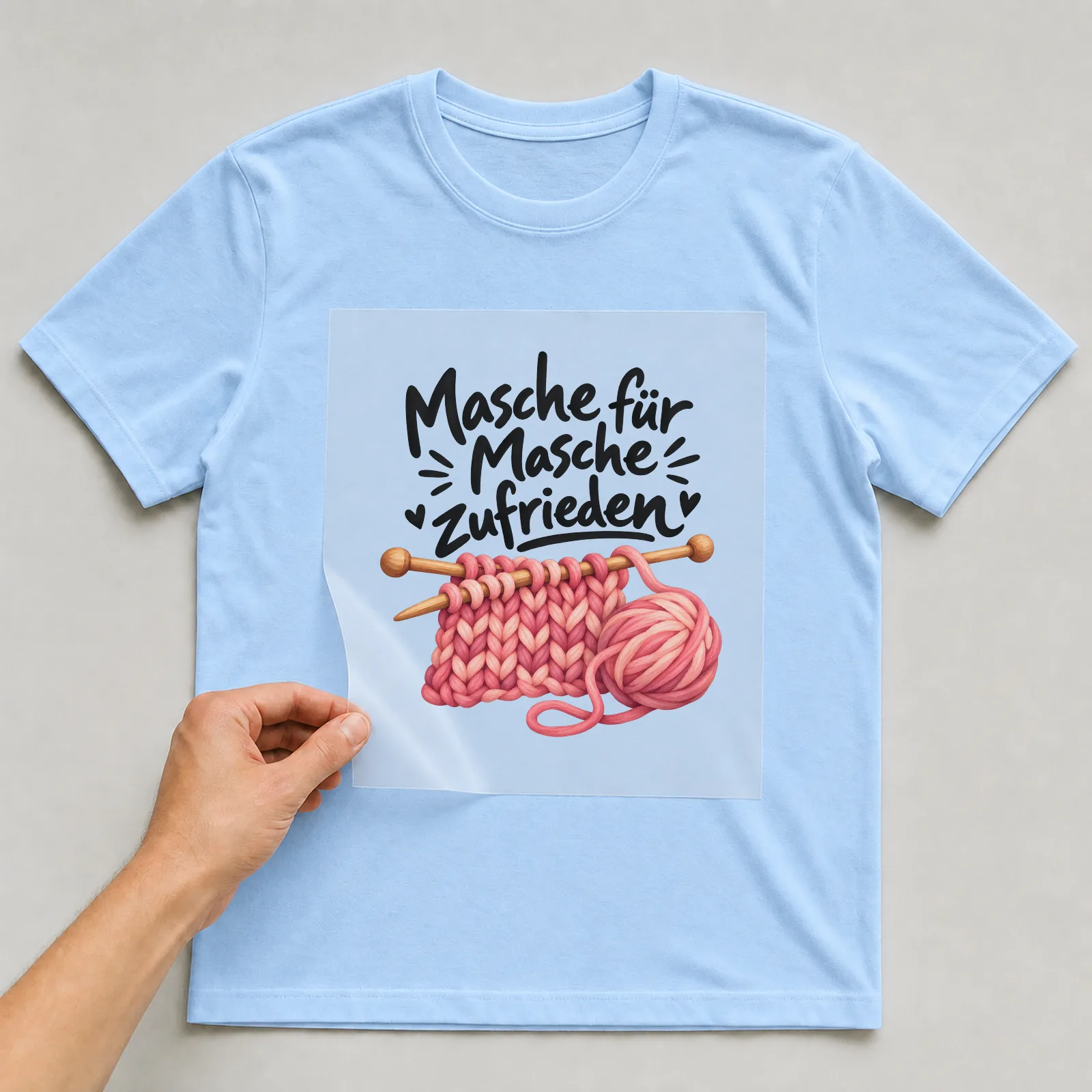 Bügelbild „Masche für Masche zufrieden“ auf hellblauem T-Shirt, Folie wird aufgelegt