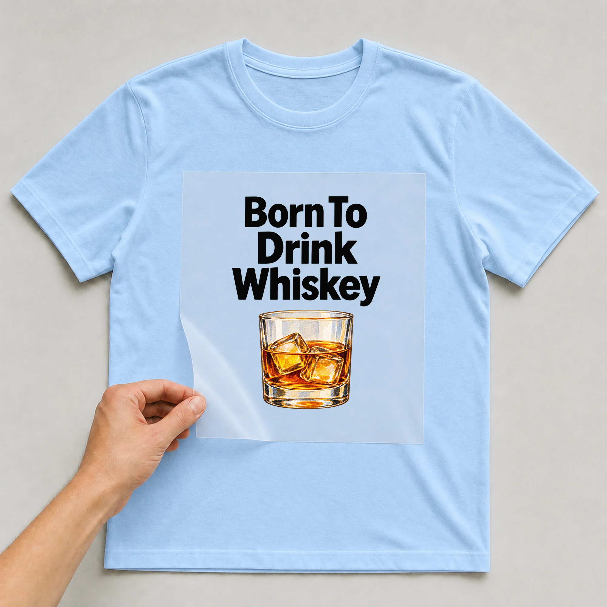 Bügelbild „Born To Drink Whiskey“ auf babyblauem T-Shirt, Folie wird aufgelegt