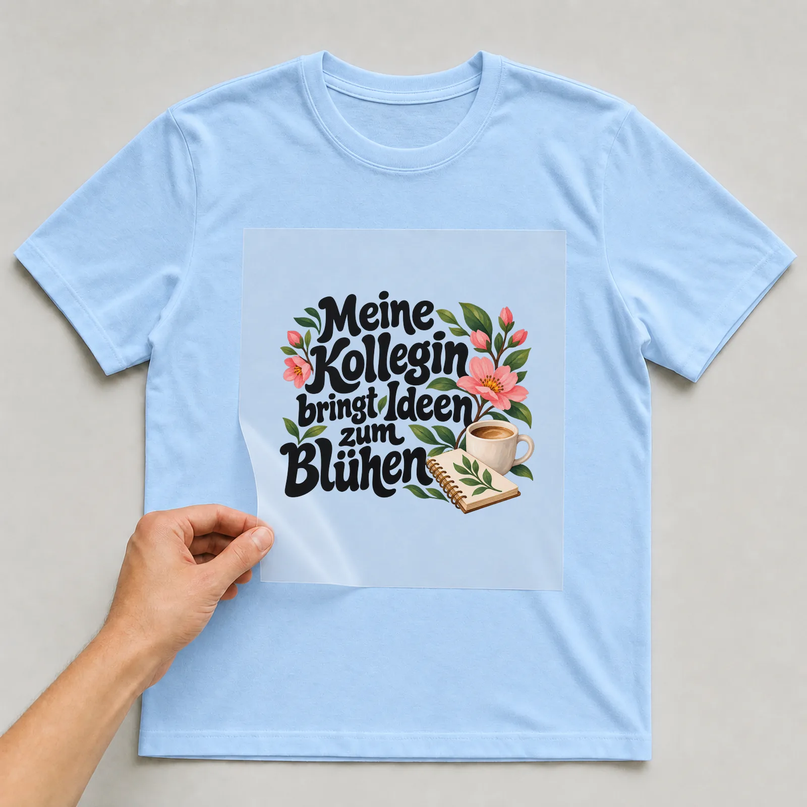 Bügelbild „Meine Kollegin bringt Ideen zum Blühen“ auf hellblauem T-Shirt, Folie wird aufgelegt