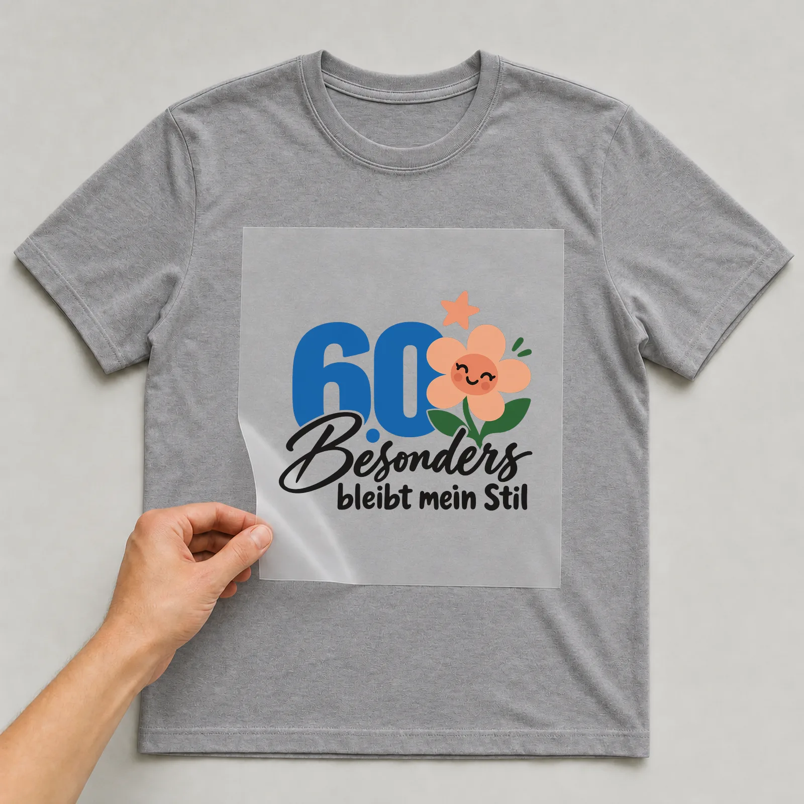 Bügelbild „60 · Besonders bleibt mein Stil“ auf grauem T-Shirt, Folie wird aufgelegt