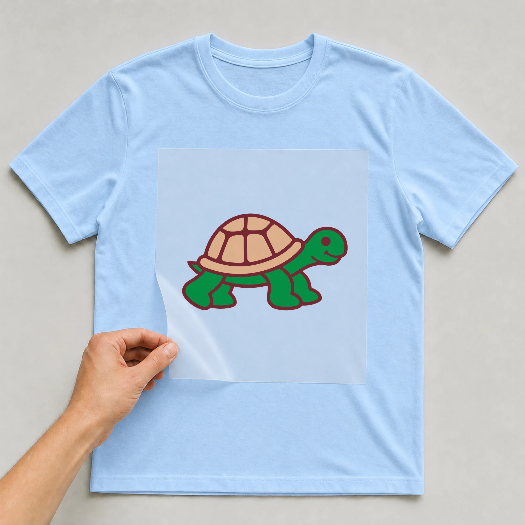 Bügelbild „Schildkröte“ auf babyblauem T-Shirt, Folie wird aufgelegt