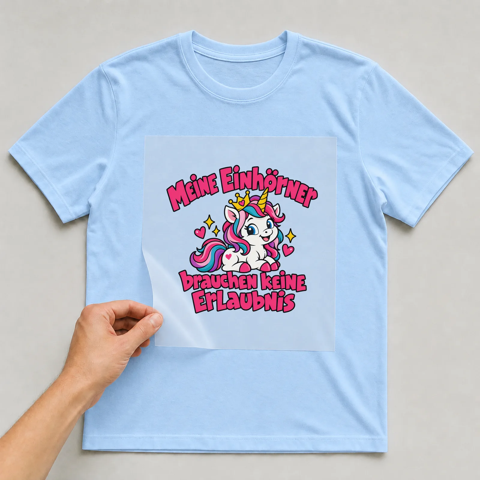 Bügelbild „Meine Einhörner brauchen keine Erlaubnis“ auf hellblauem T-Shirt, Folie wird aufgelegt