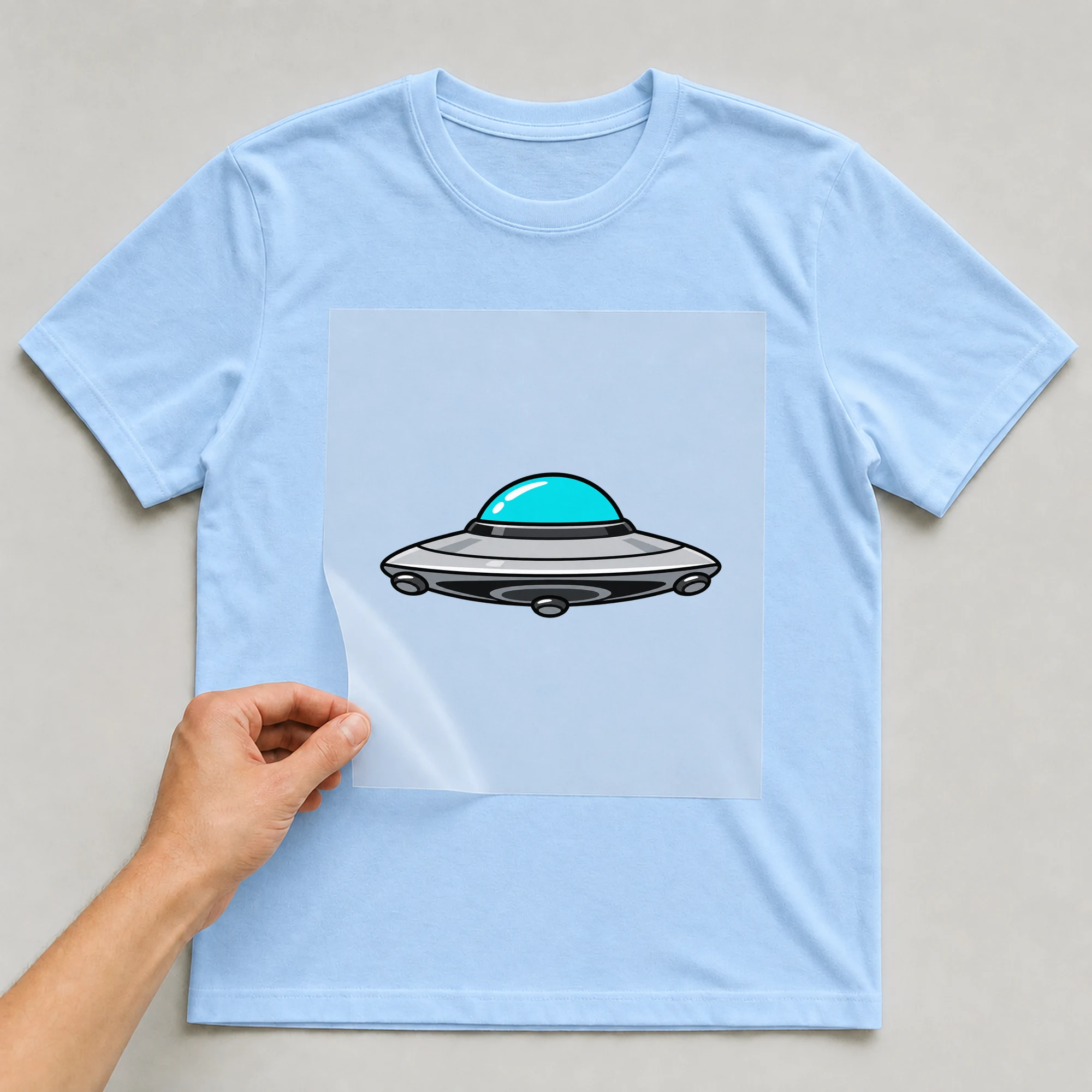 Bügelbild „UFO“ auf babyblauem T-Shirt, Folie wird aufgelegt