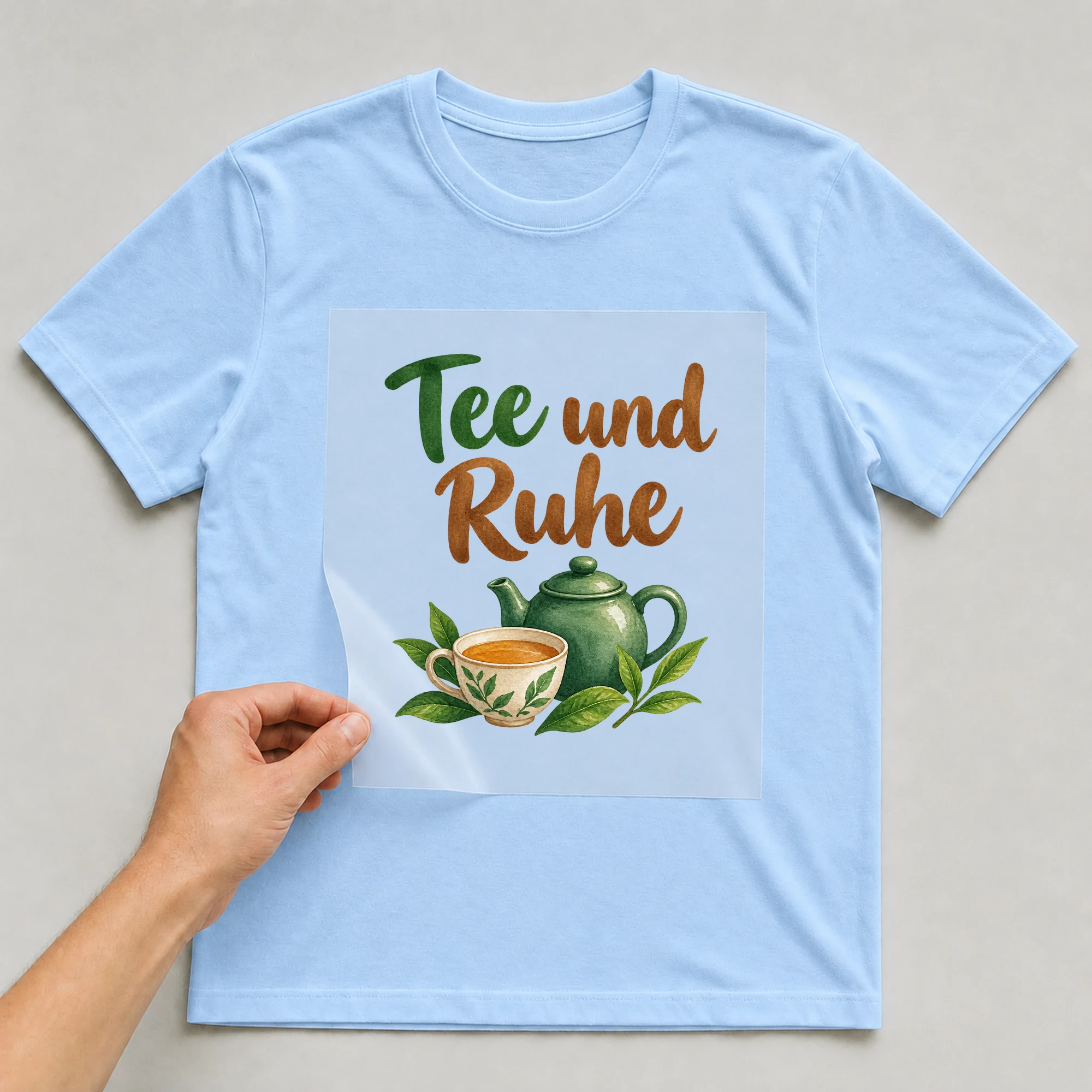 Bügelbild „Tee und Ruhe“ auf babyblauem T-Shirt, Folie wird aufgelegt