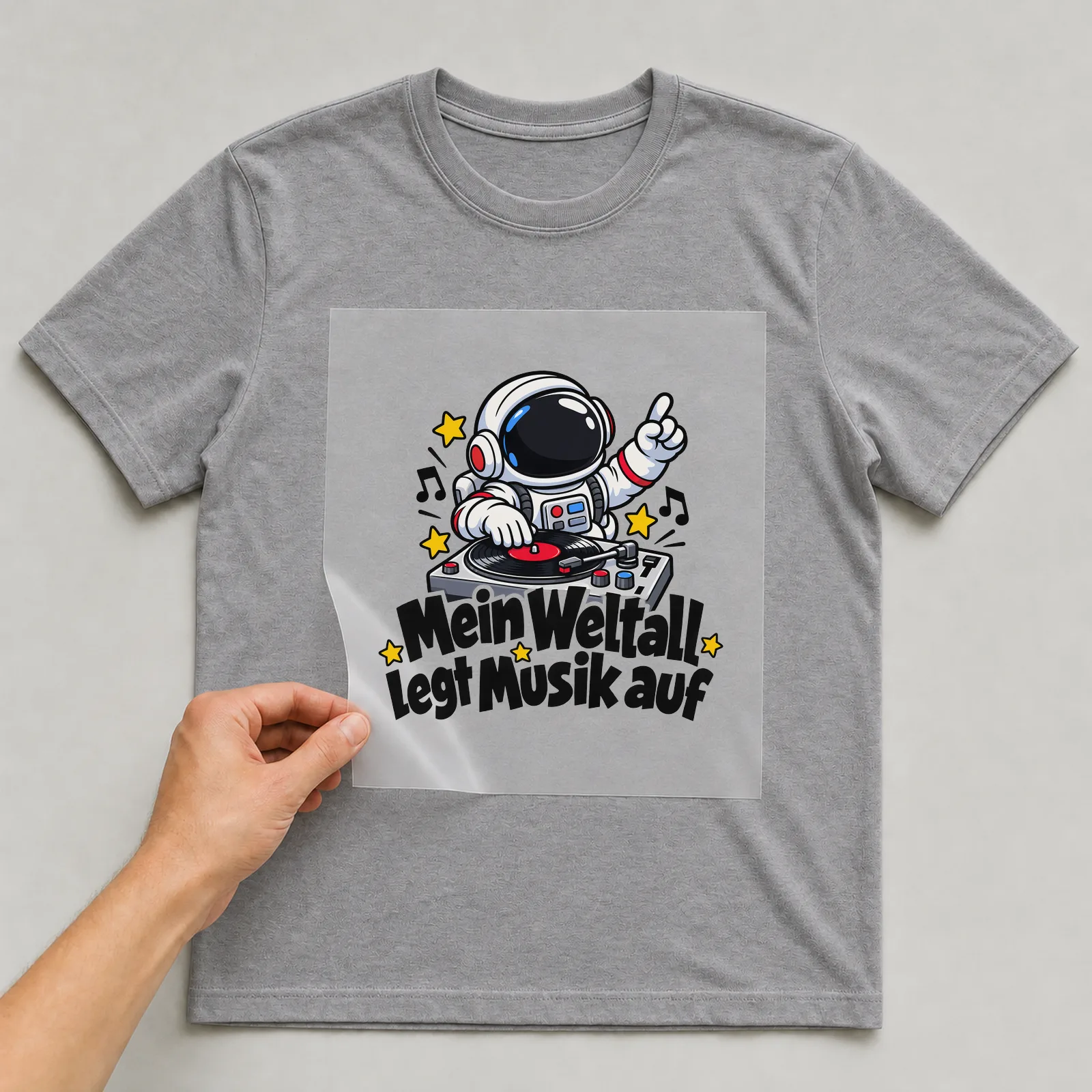 Bügelbild „Mein Weltall legt Musik auf“ auf grauem T-Shirt, Folie wird aufgelegt