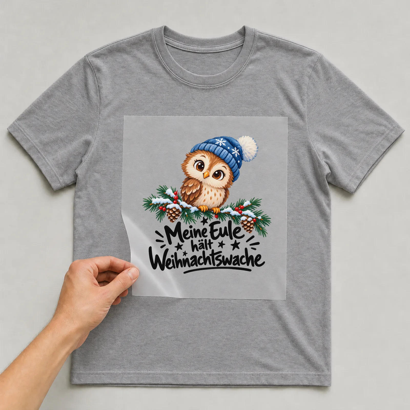 Bügelbild „Meine Eule hält Weihnachtswache“ auf grauem T-Shirt, Folie wird aufgelegt