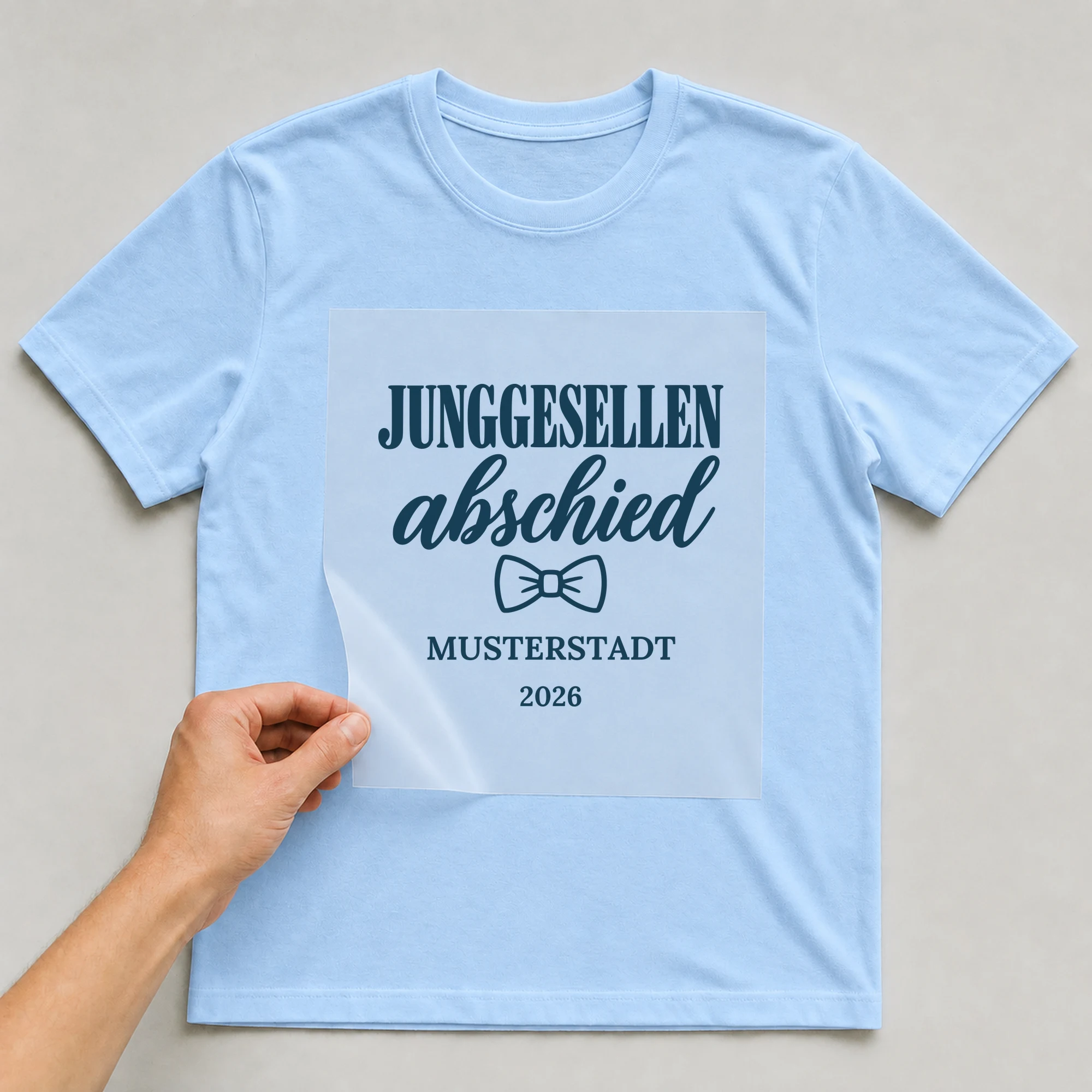 Bügelbild Junggesellenabschied mit Ort und Jahr auf hellblauem T-Shirt, Folie wird aufgelegt