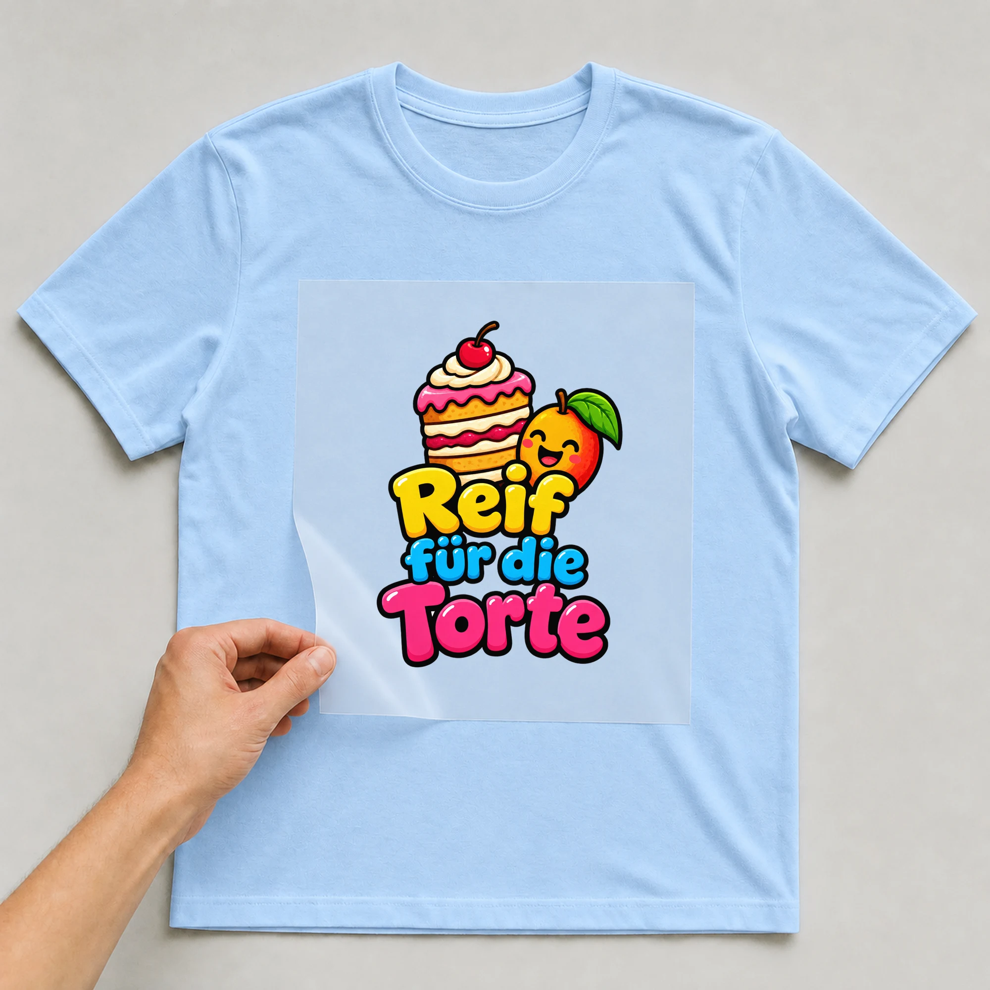 Bügelbild „Reif fuer die torte“ auf babyblauem T-Shirt, Folie wird aufgelegt