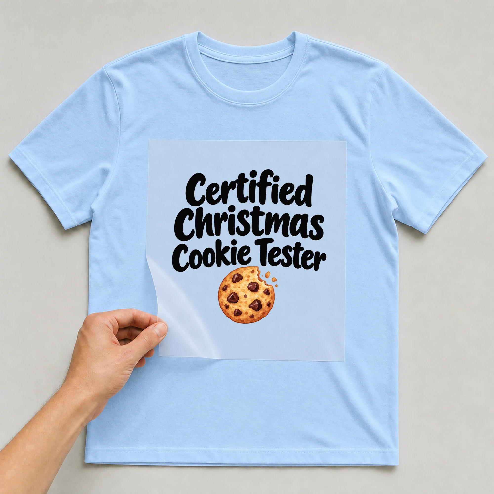 Bügelbild „Certified Christmas Cookie Tester“ auf babyblauem T-Shirt, Folie wird aufgelegt