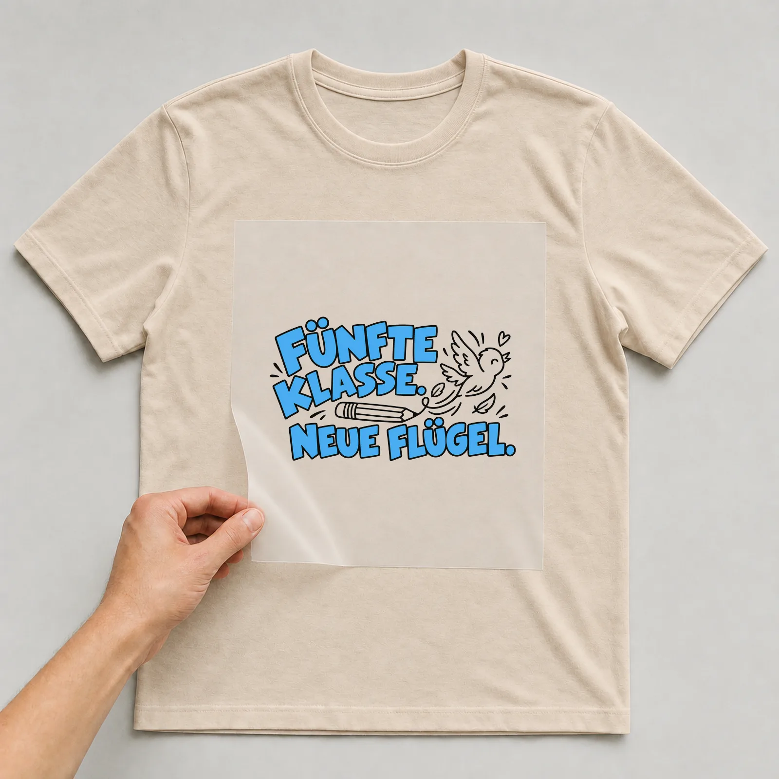 Bügelbild „Fünfte Klasse. Neue Flügel.“ auf beigem T-Shirt, Folie wird aufgelegt