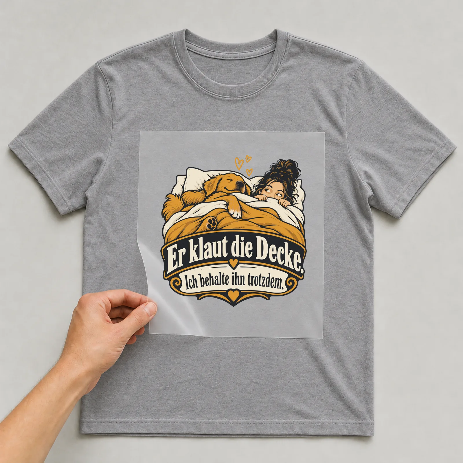 Bügelbild Er klaut die Decke. Ich behalte ihn trotzdem. (Partnermotiv) auf grauem T-Shirt, Folie wird aufgelegt