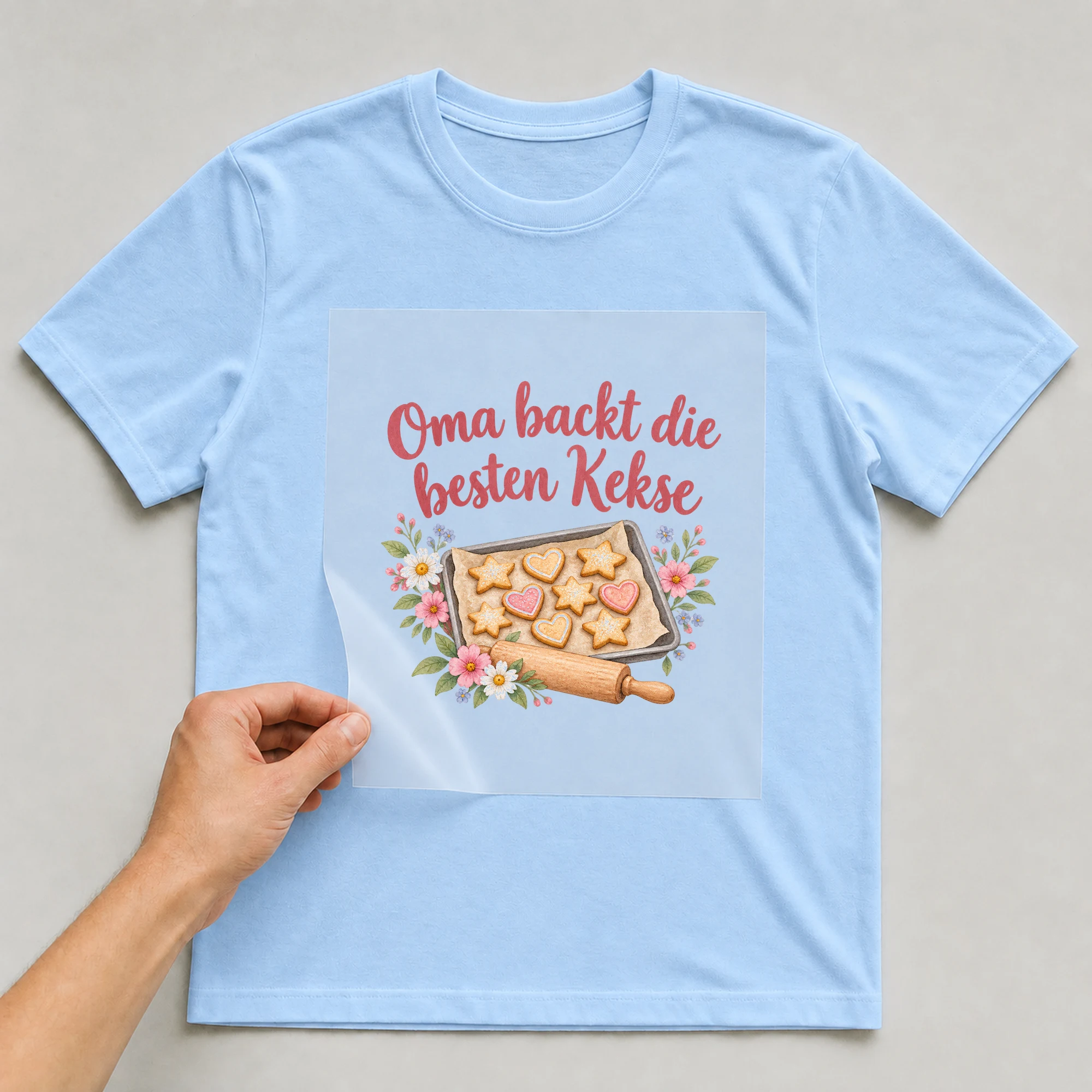 Bügelbild „Oma backt die besten Kekse“ auf babyblauem T-Shirt, Folie wird aufgelegt