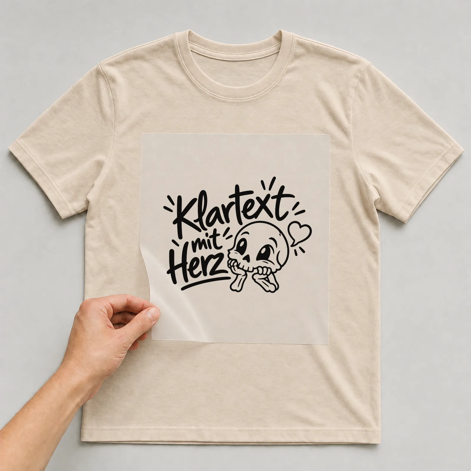 Bügelbild „Klartext mit Herz“ (klaren Konturen) auf beigem T-Shirt, Folie wird aufgelegt