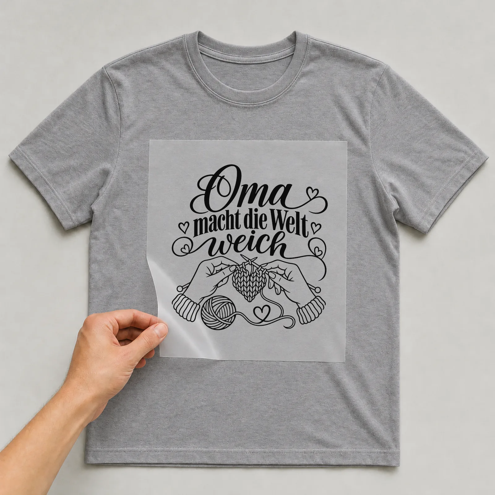 Bügelbild „Oma macht die Welt weich“ auf grauem T-Shirt, Folie wird aufgelegt
