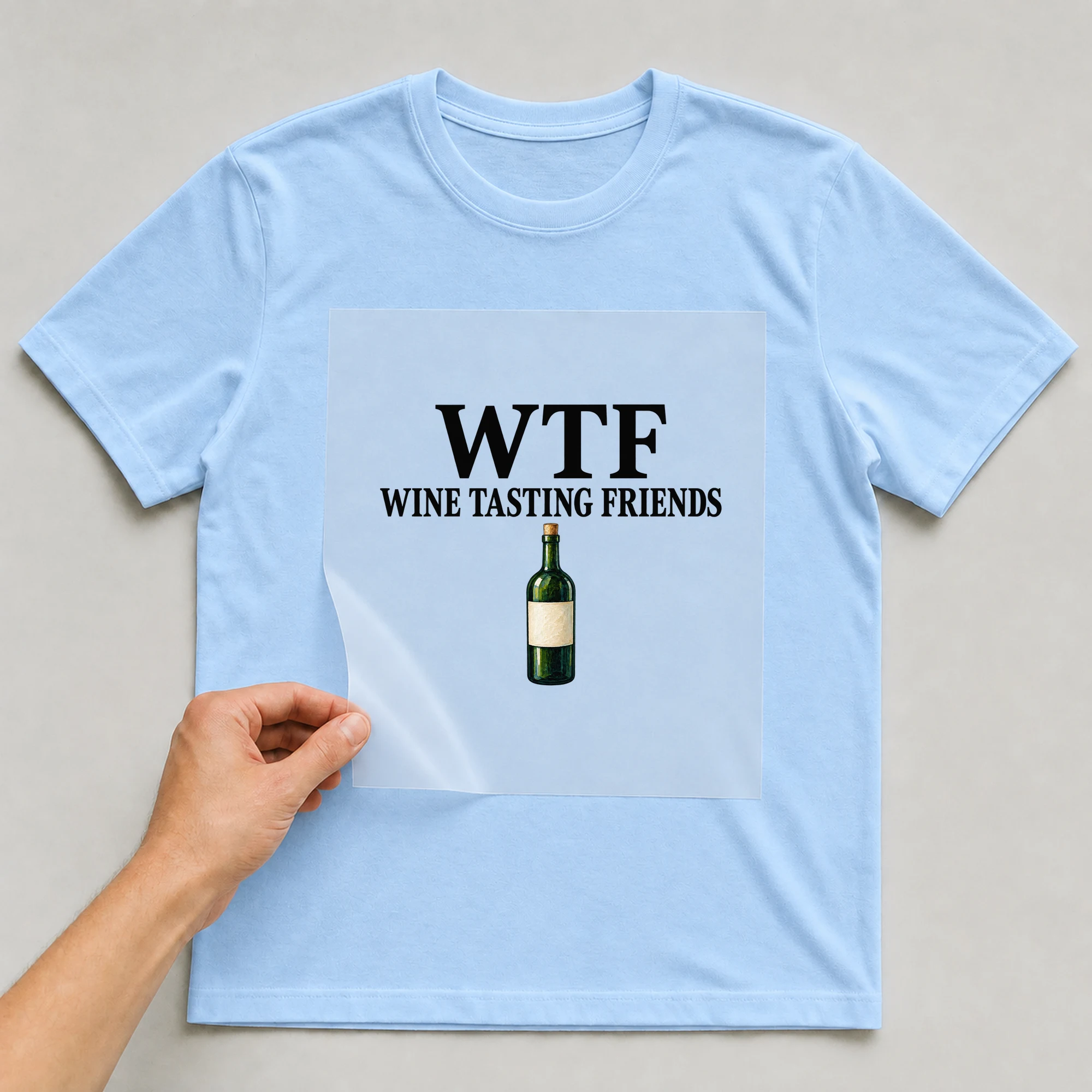Bügelbild „WTF WINE TASTING FRIENDS“ auf babyblauem T-Shirt, Folie wird aufgelegt