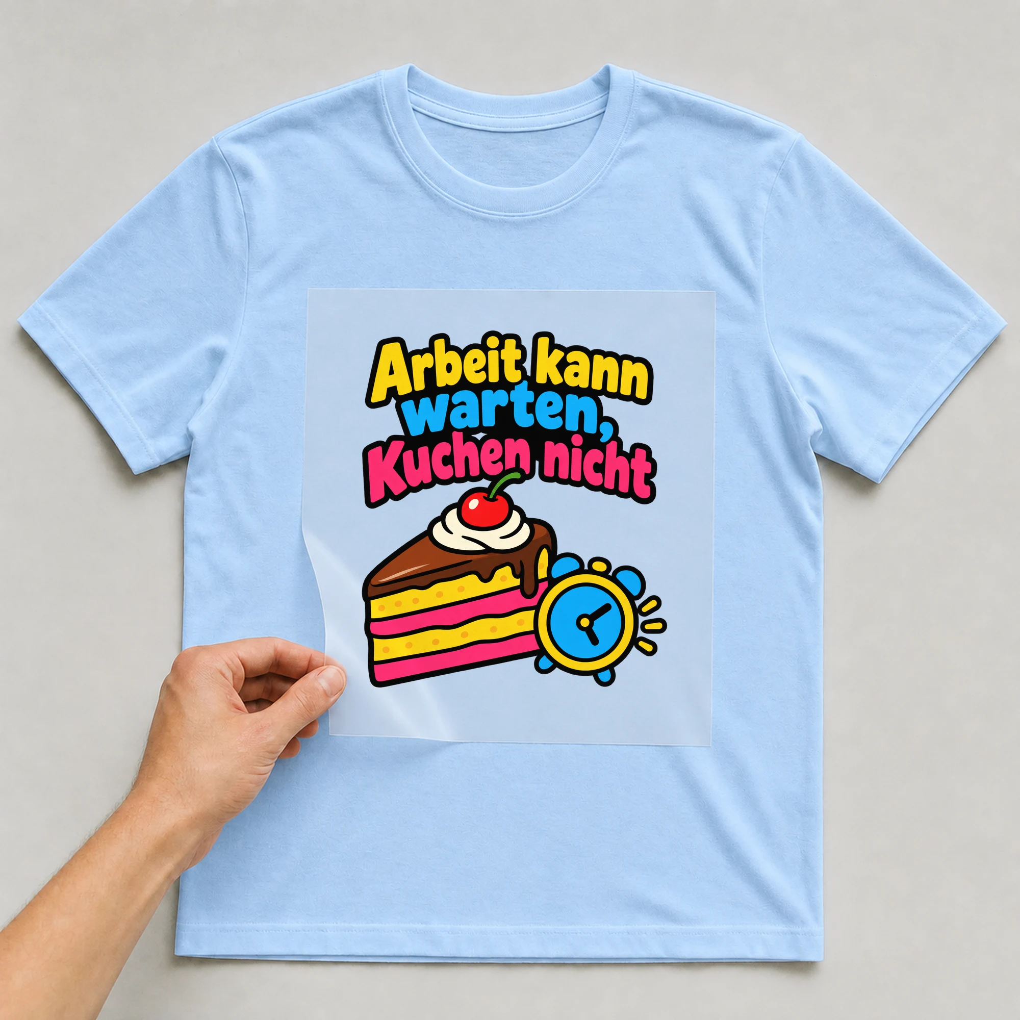 Bügelbild „Arbeit kann warten, Kuchen nicht“ auf babyblauem T-Shirt, Folie wird aufgelegt