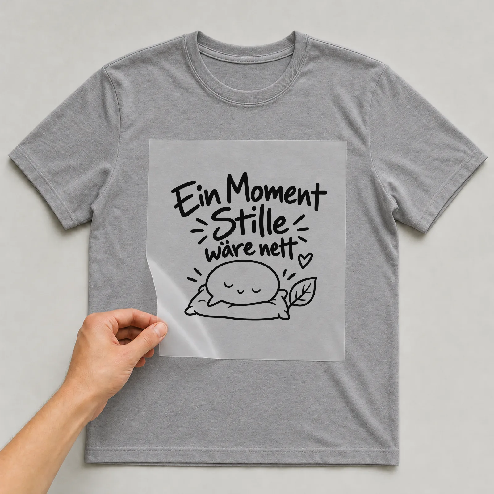Bügelbild „Ein Moment Stille wäre nett“ auf grauem T-Shirt, Folie wird aufgelegt