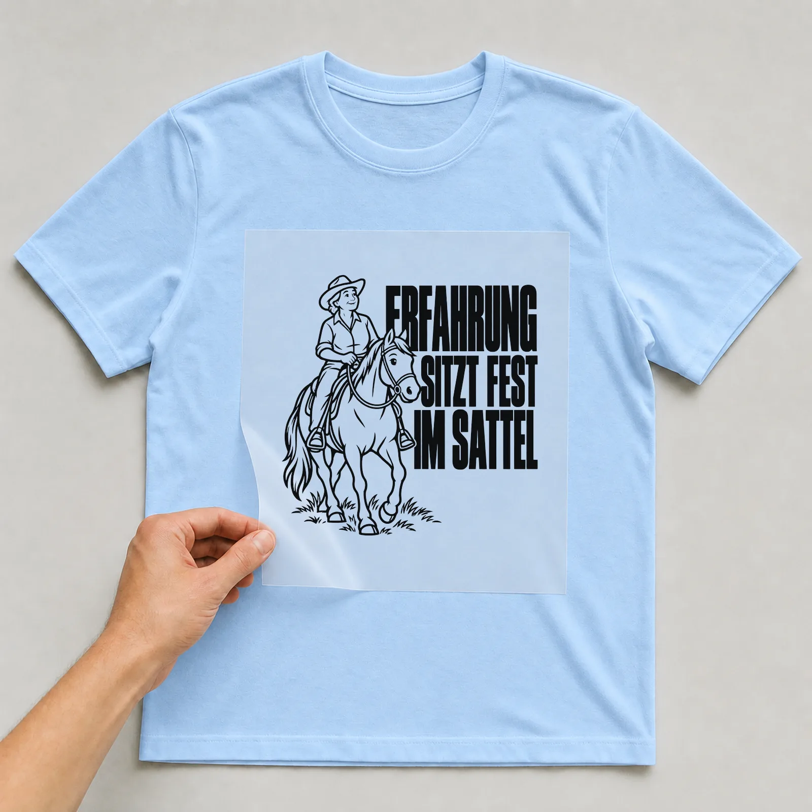 Bügelbild „Erfahrung sitzt fest im Sattel“ auf hellblauem T-Shirt, Folie wird aufgelegt