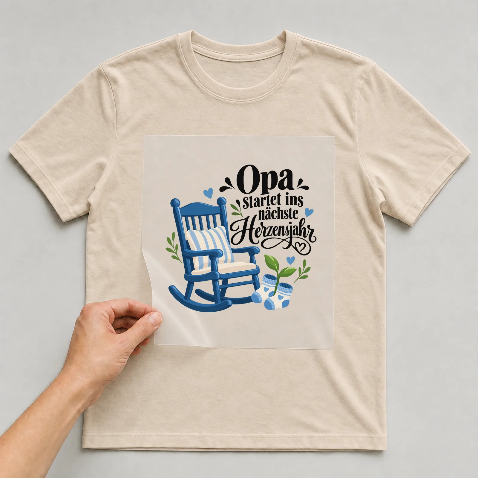 Bügelbild „Opa startet ins nächste Herzensjahr“ auf beigem T-Shirt, Folie wird aufgelegt