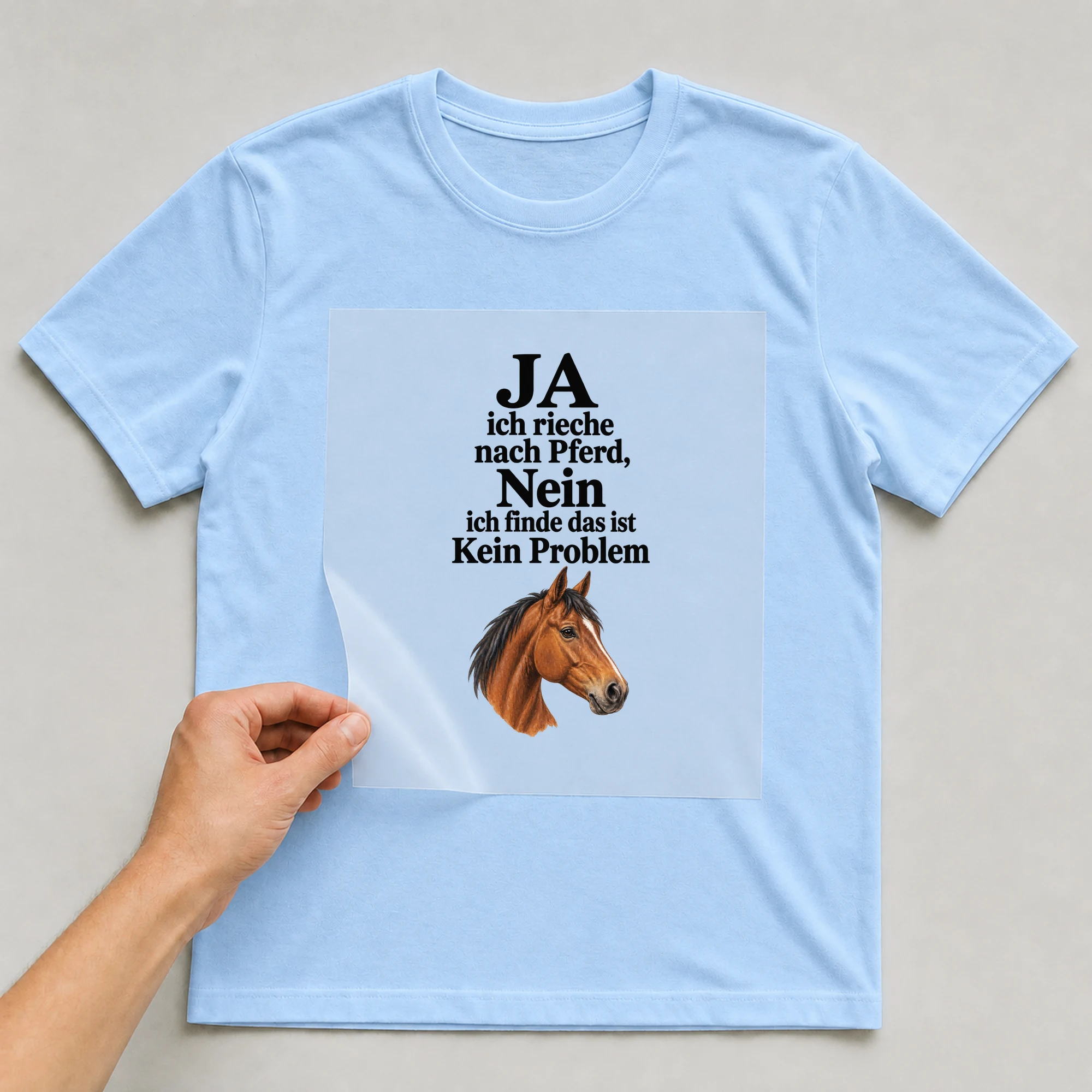 Bügelbild „JA ich rieche nach Pferd, Nein ich finde das ist Kein Problem“ auf babyblauem T-Shirt, Folie wird aufgelegt